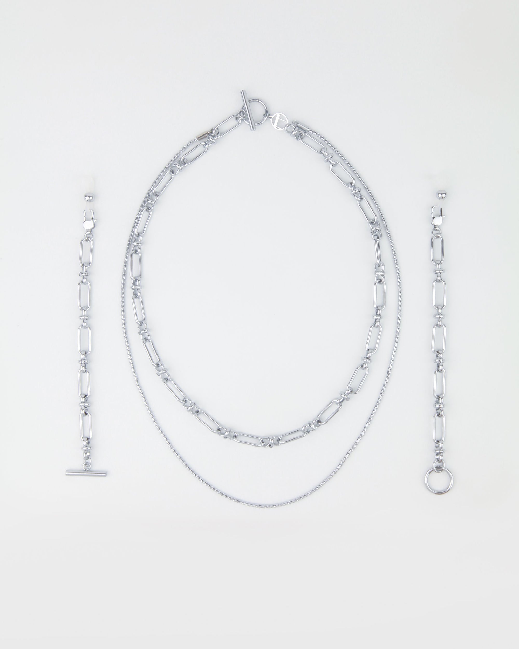 A Vienna Glasses Chain by For Art&#39;s Sake®, featuring an oval link necklace with a toggle clasp, a shorter fine chain necklace, a bracelet with a toggle clasp, and a bracelet with a ring clasp—all arranged neatly on a light background. The collection&#39;s 18-karat gold-plating adds an elegant touch to each piece.