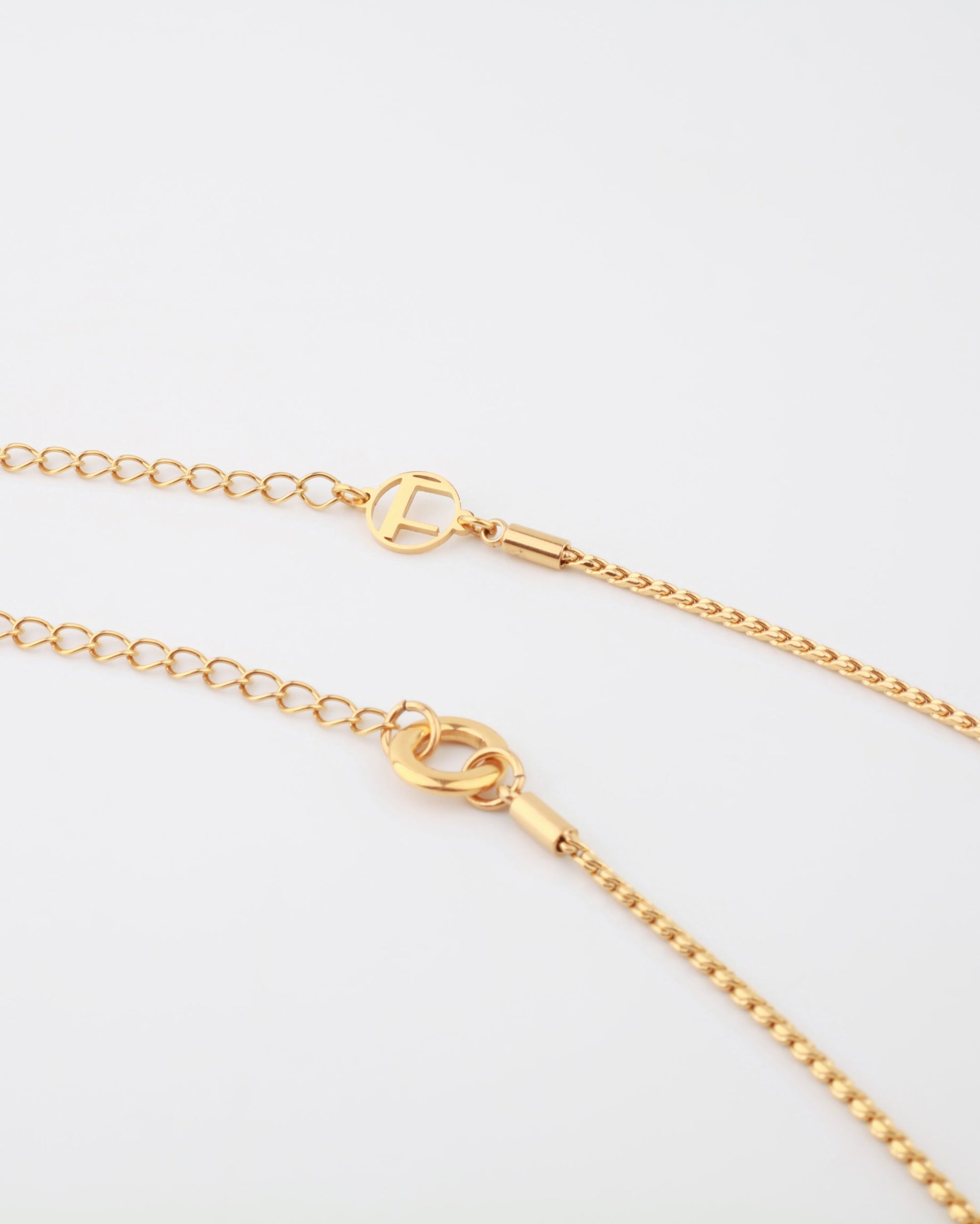 A Miami Glasses Chain by For Art's Sake® is shown against a white background. It features an elegant design with a circular charm with a cut-out 'T' and a lobster clasp for fastening. A small extender chain is also visible, allowing for adjustable length.