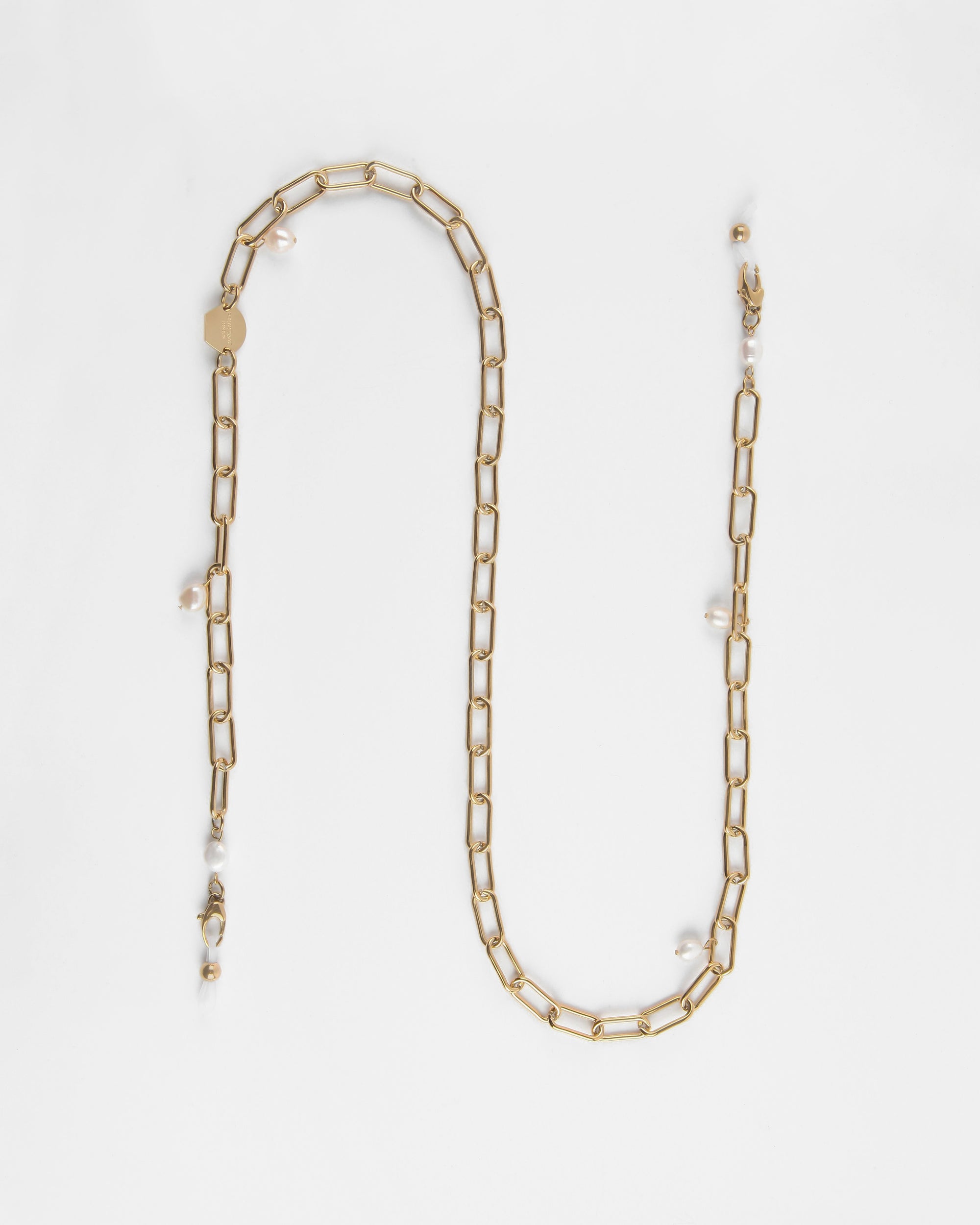 A Marylebone Glasses Chain with rectangular links, embellished with small freshwater pearls interspersed along its length. The 18K gold-plated chain from For Art's Sake® is laid out in a loose curve against a plain white background, showing its simplicity and elegance.