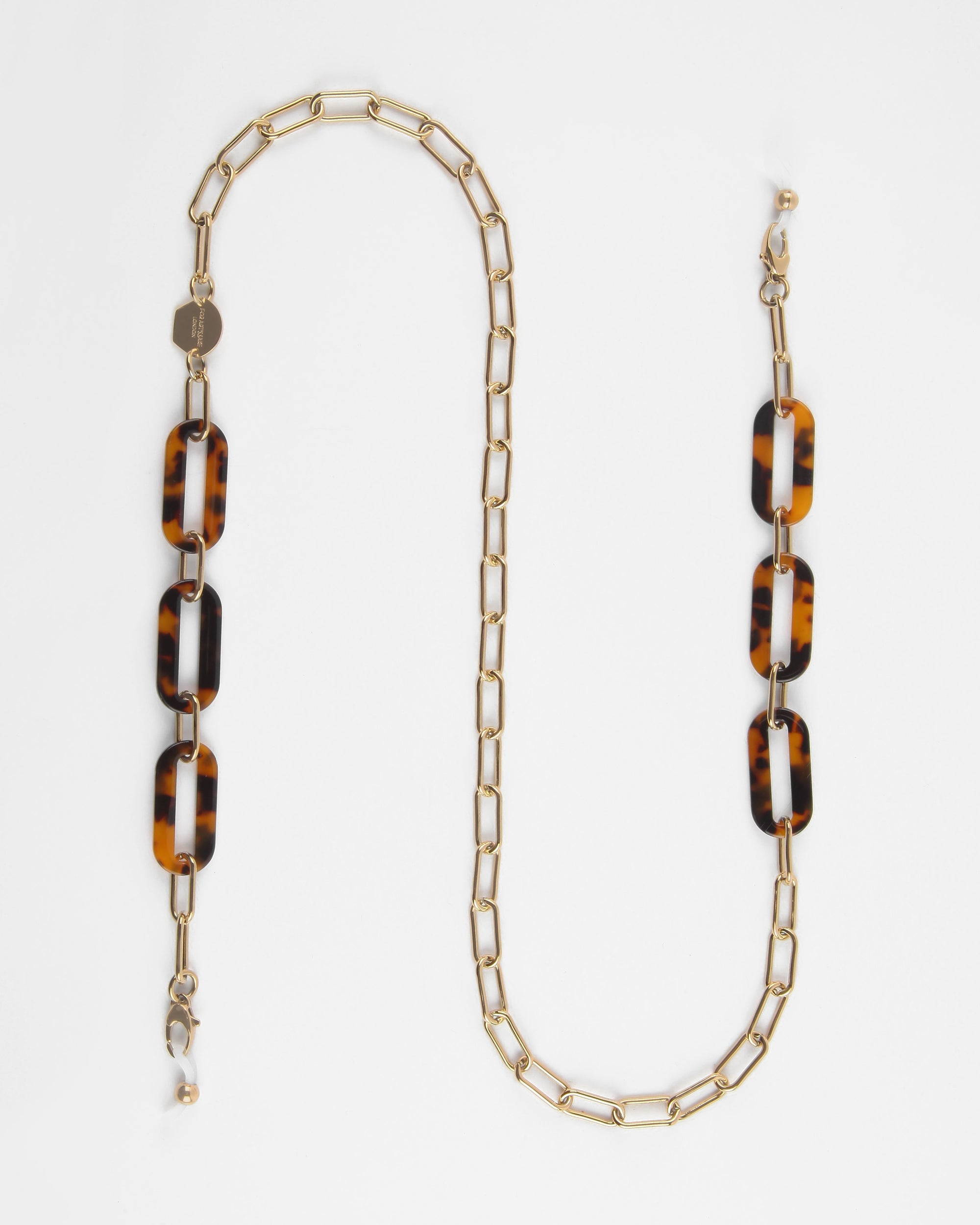 A stylish eyeglass chain with 18K gold-plated rectangular links and four tortoiseshell-patterned resin links. The clasp at each end allows for easy attachment to eyeglasses. This For Art&#39;s Sake® Kensington Glasses Chain design is modern and elegant, suitable for both functional use and as a fashion accessory.