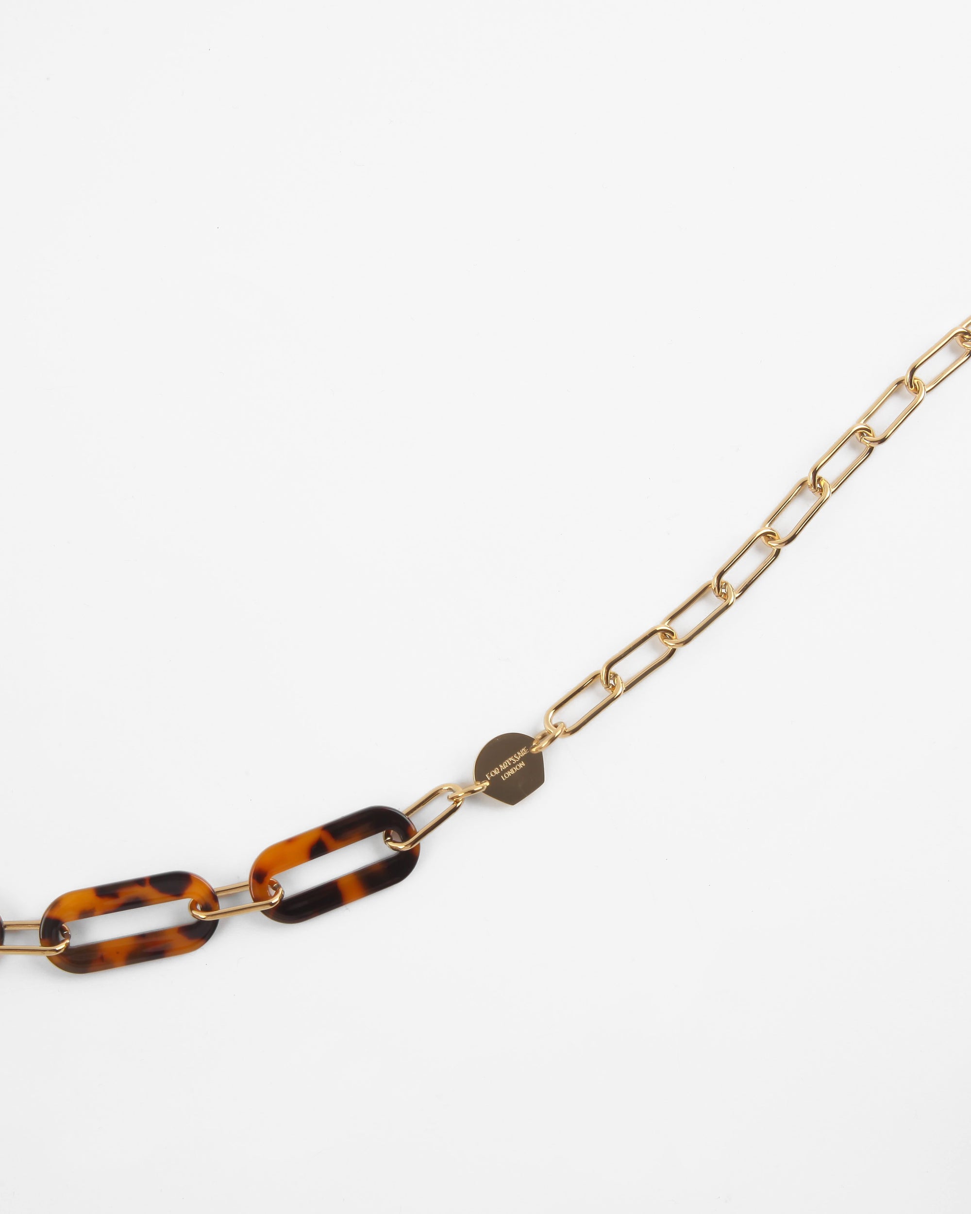 Close-up of a Kensington Glasses Chain by For Art's Sake® with a mixture of gold rectangular links and tortoiseshell-patterned Italian acetate links. The chain also features a small, heart-shaped charm. The necklace is displayed on a plain white background.