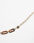 Close-up of a Kensington Glasses Chain by For Art's Sake® with a mixture of gold rectangular links and tortoiseshell-patterned Italian acetate links. The chain also features a small, heart-shaped charm. The necklace is displayed on a plain white background.