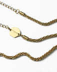 Close-up of an 18k gold-plated Mayfair Glasses Chain by For Art's Sake® featuring intricate woven links. The chain has an adjustable, heart-shaped claw closure and a small hexagonal tag engraved with the words "FOR ART'S SAKE." The background is white, highlighting the exquisite details of the chain and tag.