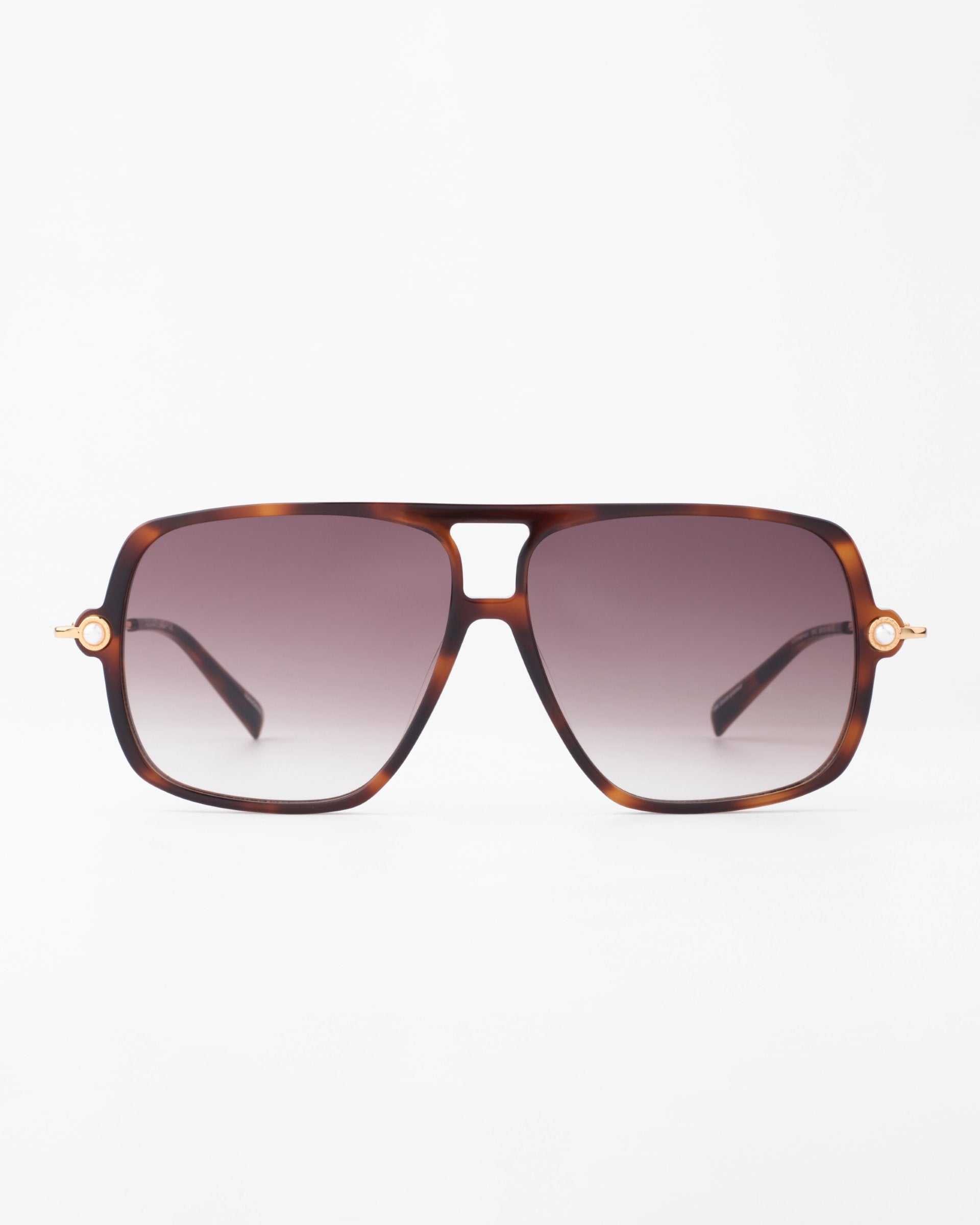 The Cinnamon by For Art&#39;s Sake® is a pair of square-shaped sunglasses with a prominent browline and thick tortoiseshell frames, featuring gradient lenses that darken from light at the bottom to darker at the top. The arms taper towards the ear and showcase small metal accents with faux pearl embellishment.
