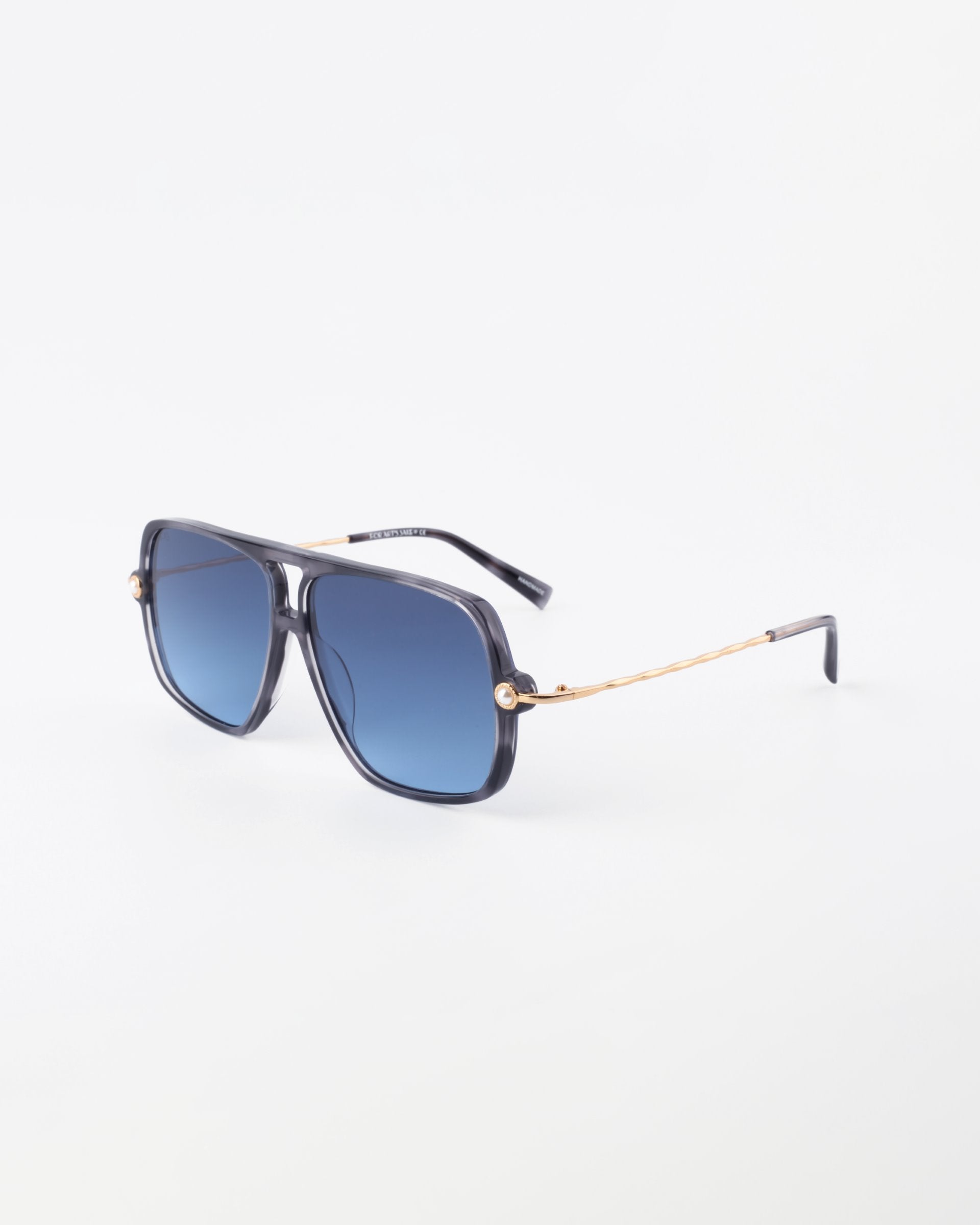 A pair of stylish sunglasses with black square frames, 18-karat gold-plated temples, and blue gradient lenses. The design features thin, wavy gold lines along the arms and small decorative elements near the hinges, adding a touch of elegance to the eyewear. This is *Cinnamon* by *For Art&#39;s Sake®*.