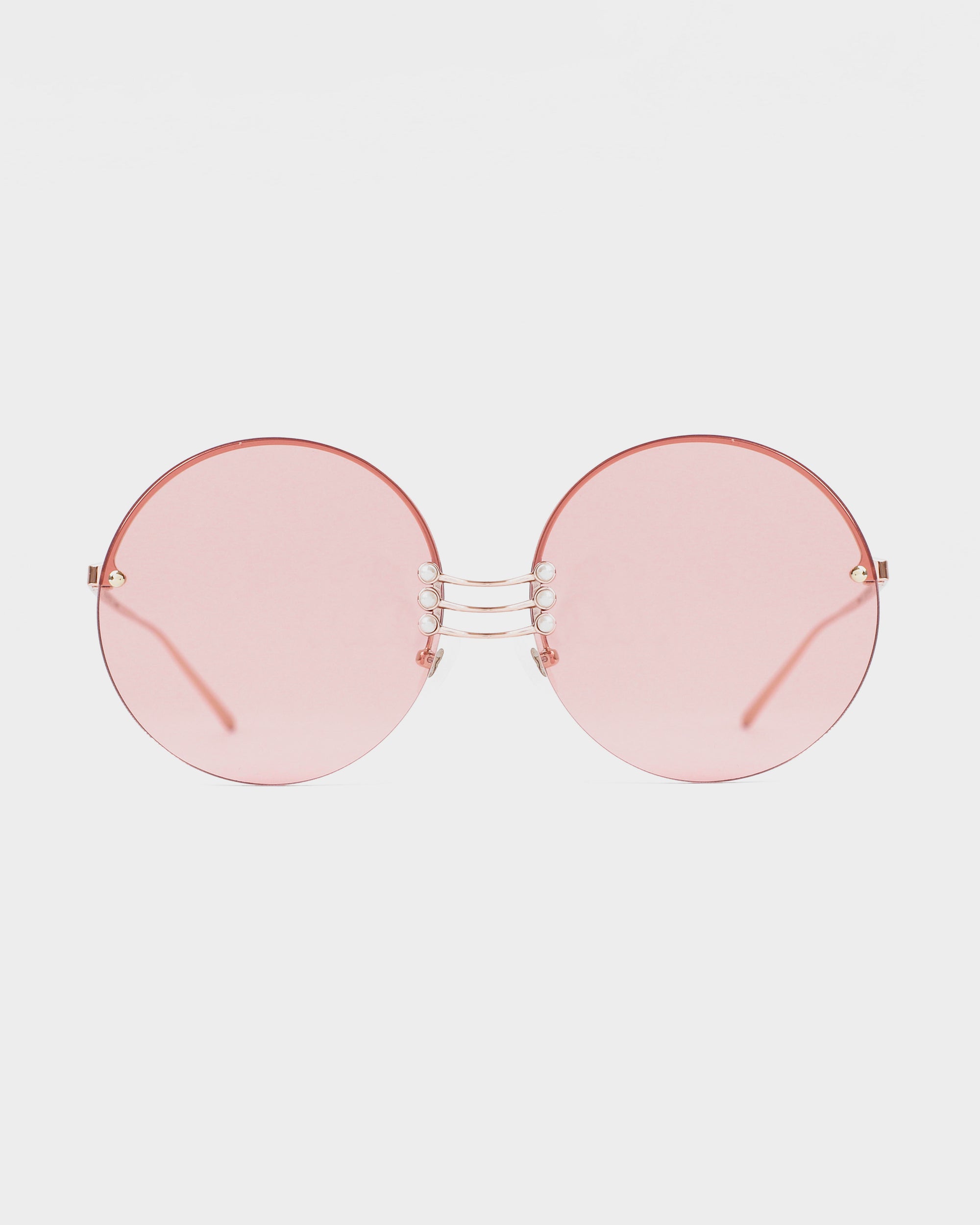 A pair of round, rimless For Art&#39;s Sake® Vermeer sunglasses with pink-tinted lenses. Featuring UV protection, the sunglasses boast gold-toned bridge and temple arms, stainless steel frames, and a unique nose bridge design with three parallel thin bars. Gemstone nosepads add a touch of elegance. The background is plain white.