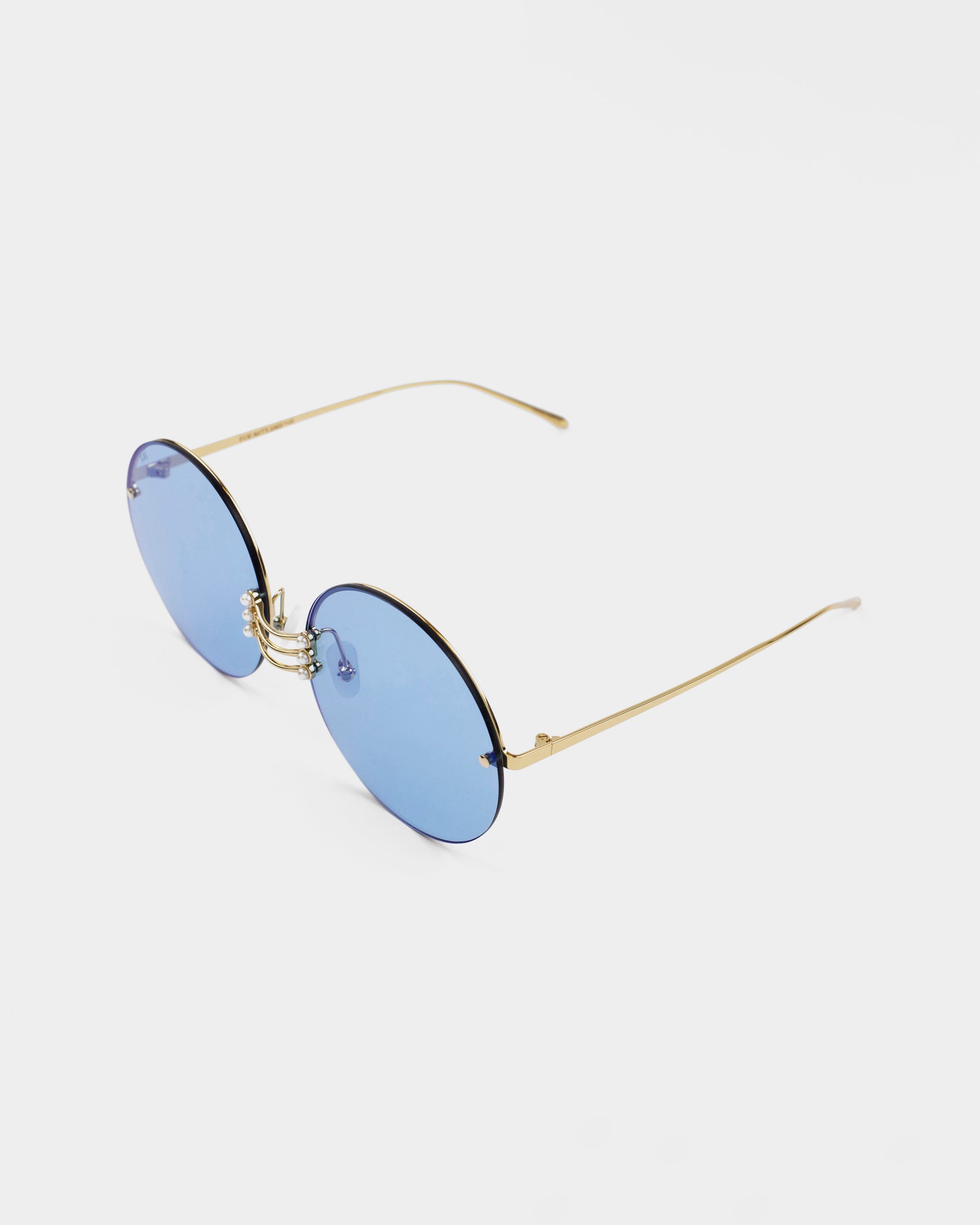 A pair of stylish For Art&#39;s Sake® Vermeer sunglasses with round blue lenses and slender stainless steel frames. The temples are straight and also gold, providing a minimalist yet elegant design. The gemstone nosepads add a touch of luxury, while the UV protection ensures your eyes stay safe. The background is plain white, highlighting the sleek and modern appearance of the sunglasses.