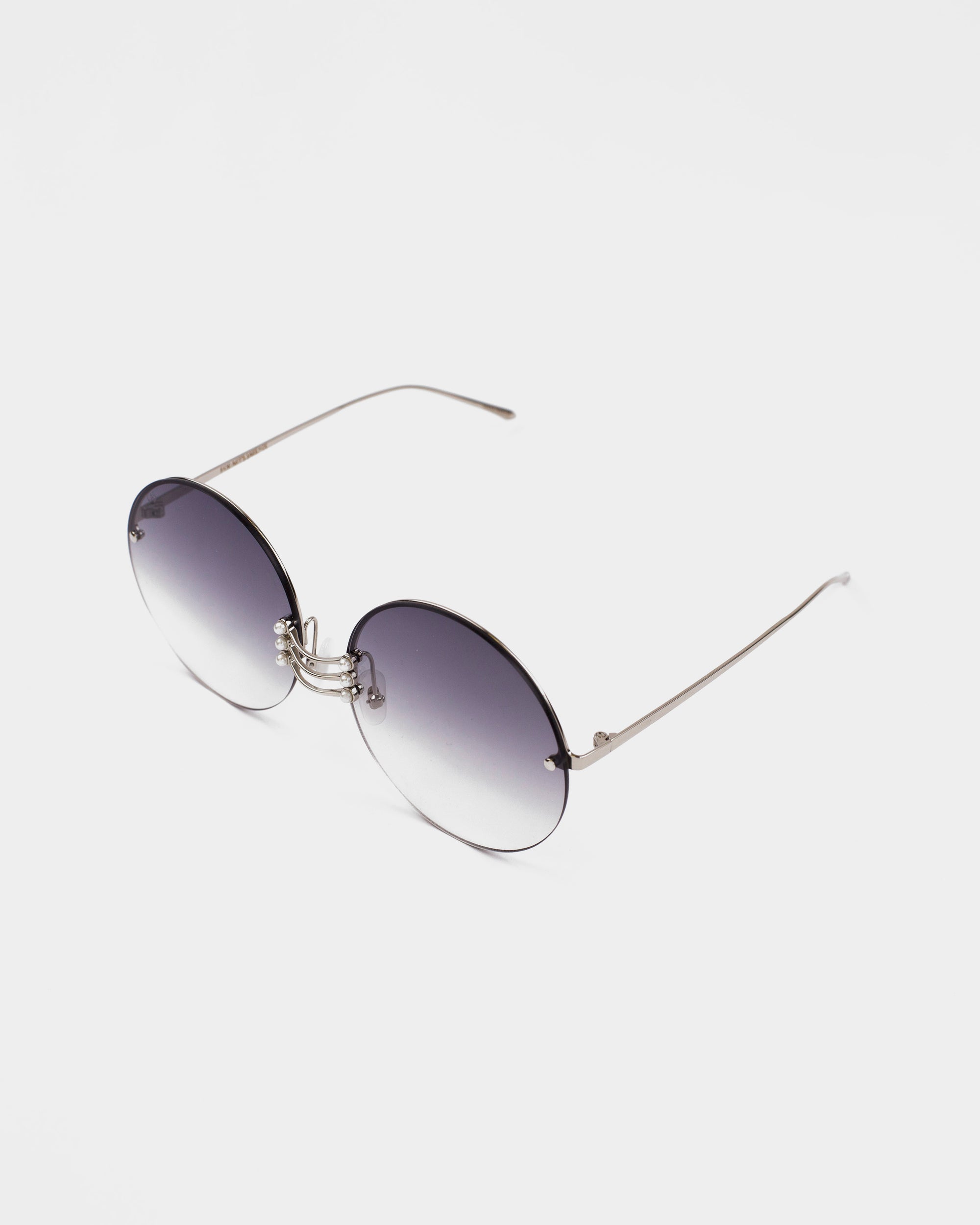 A pair of Vermeer sunglasses by For Art&#39;s Sake® with dark grey gradient lenses and thin stainless steel frames. The sunglasses are positioned on a white background, displayed at a slight angle. The UV protection lenses ensure comfort, while the gemstone nose pads add a touch of elegance.