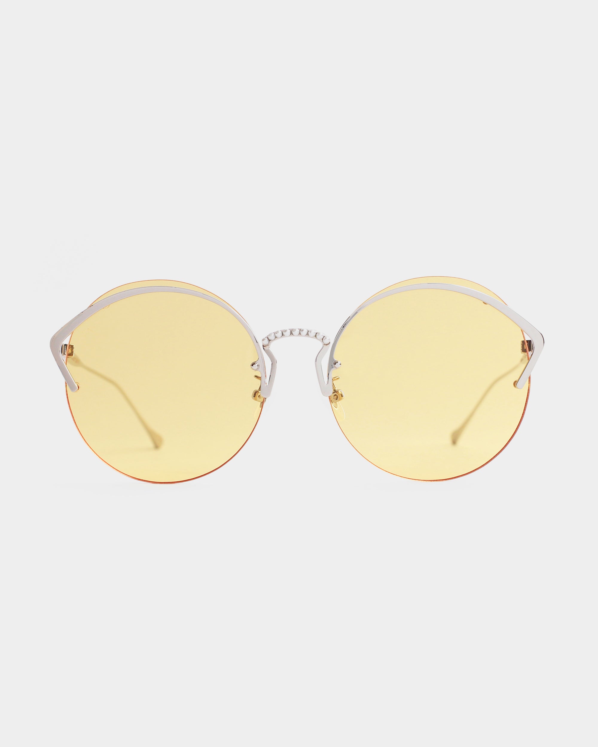 A pair of Margarita sunglasses by For Art's Sake® with yellow-tinted nylon lenses and a stainless steel frame. The sunglasses feature thin, curved temples and a unique bridge design, ensuring both UV protection and stylish appeal. The background is plain white.