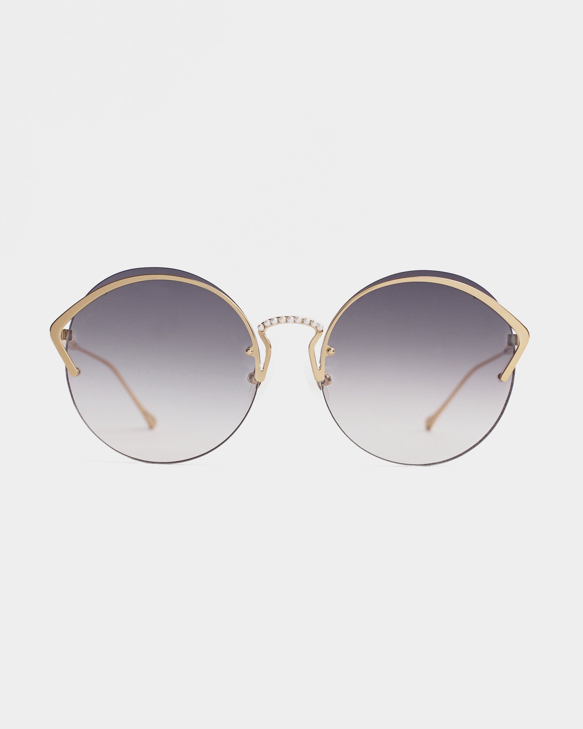 A pair of stylish round sunglasses with gradient nylon lenses fading from dark at the top to light at the bottom. The frame is gold-toned stainless steel featuring intricate metalwork near the hinges, and the nose bridge sports a small bar design, providing essential UV protection. The background is plain white. Introducing Margarita by For Art's Sake®.