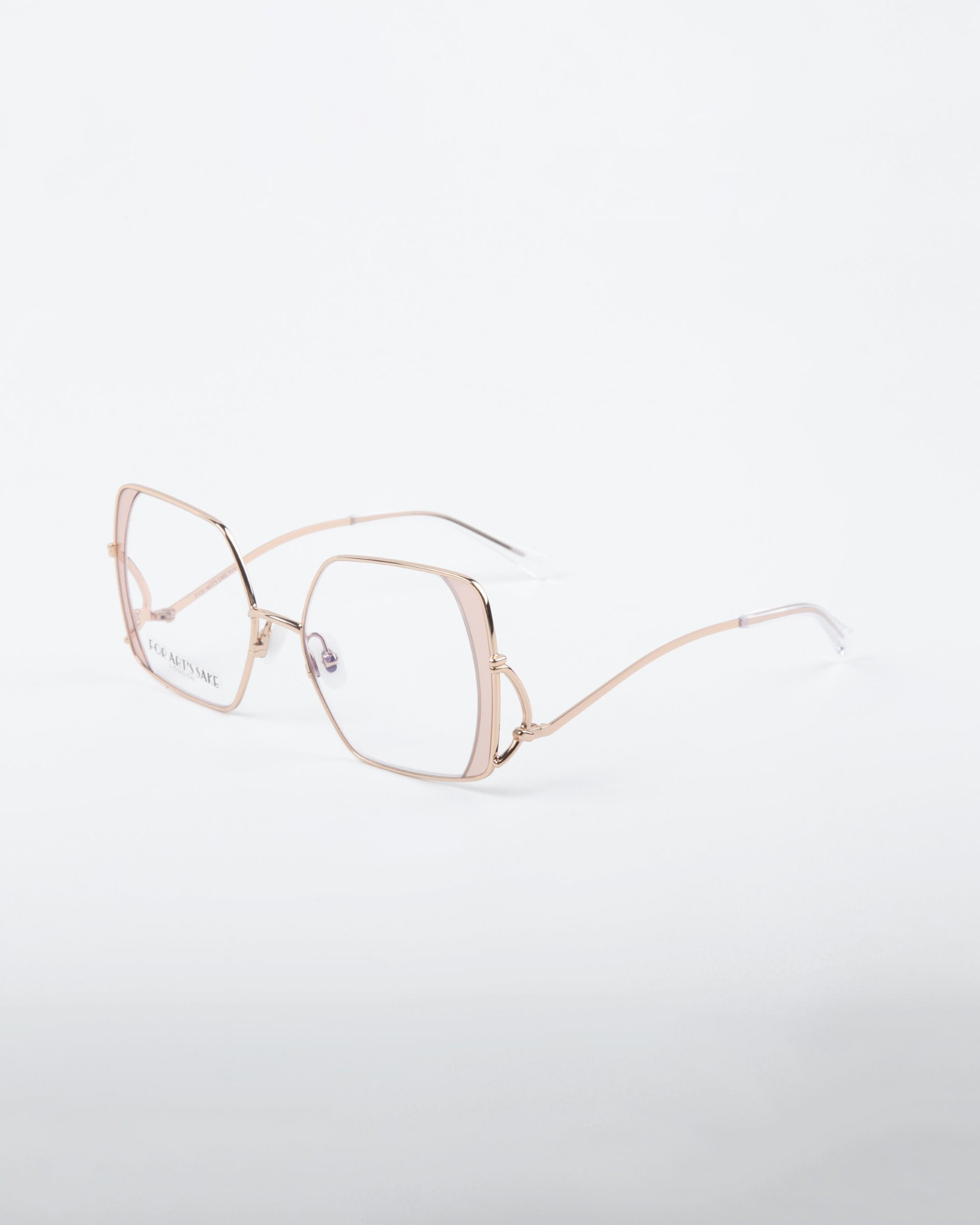 A pair of gold-rimmed, geometric eyeglasses with clear lenses is displayed on a plain white background. The Candy glasses from For Art&#39;s Sake® feature distinctive angular frames, thin, delicate arms, and are crafted from high-quality stainless steel.