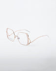 A pair of gold-rimmed, geometric eyeglasses with clear lenses is displayed on a plain white background. The Candy glasses from For Art's Sake® feature distinctive angular frames, thin, delicate arms, and are crafted from high-quality stainless steel.