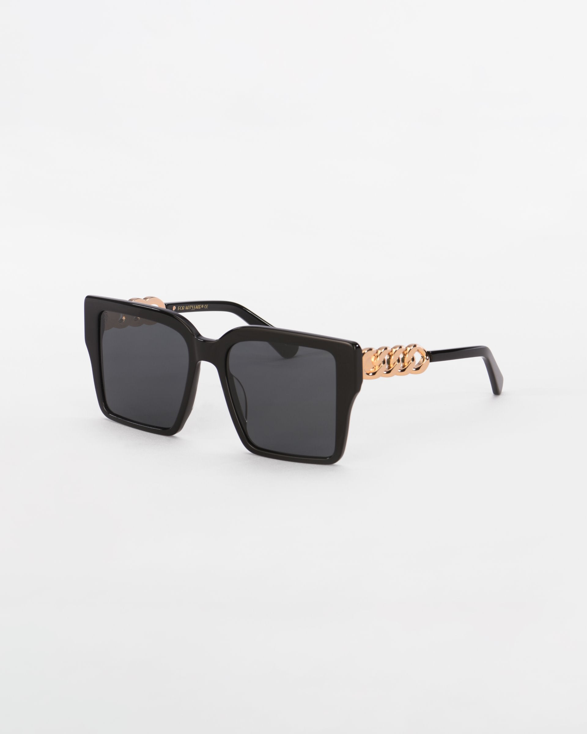 A pair of stylish black oversized square sunglasses named Castle from For Art&#39;s Sake® with ultra-lightweight dark lenses against a white background. The temples are adorned with an 18-karat gold plated chain detail, adding a touch of elegance to the modern design.