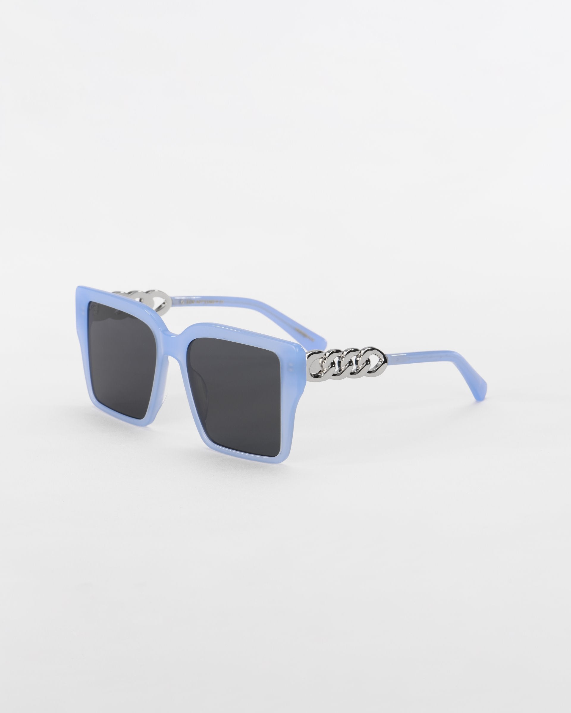 A pair of stylish, oversized square-shaped **Castle** sunglasses with light blue frames and ultra-lightweight dark lenses by **For Art&#39;s Sake®**. The arms feature an 18-karat gold plated chain detail near the hinges. The sunglasses are set against a plain white background.