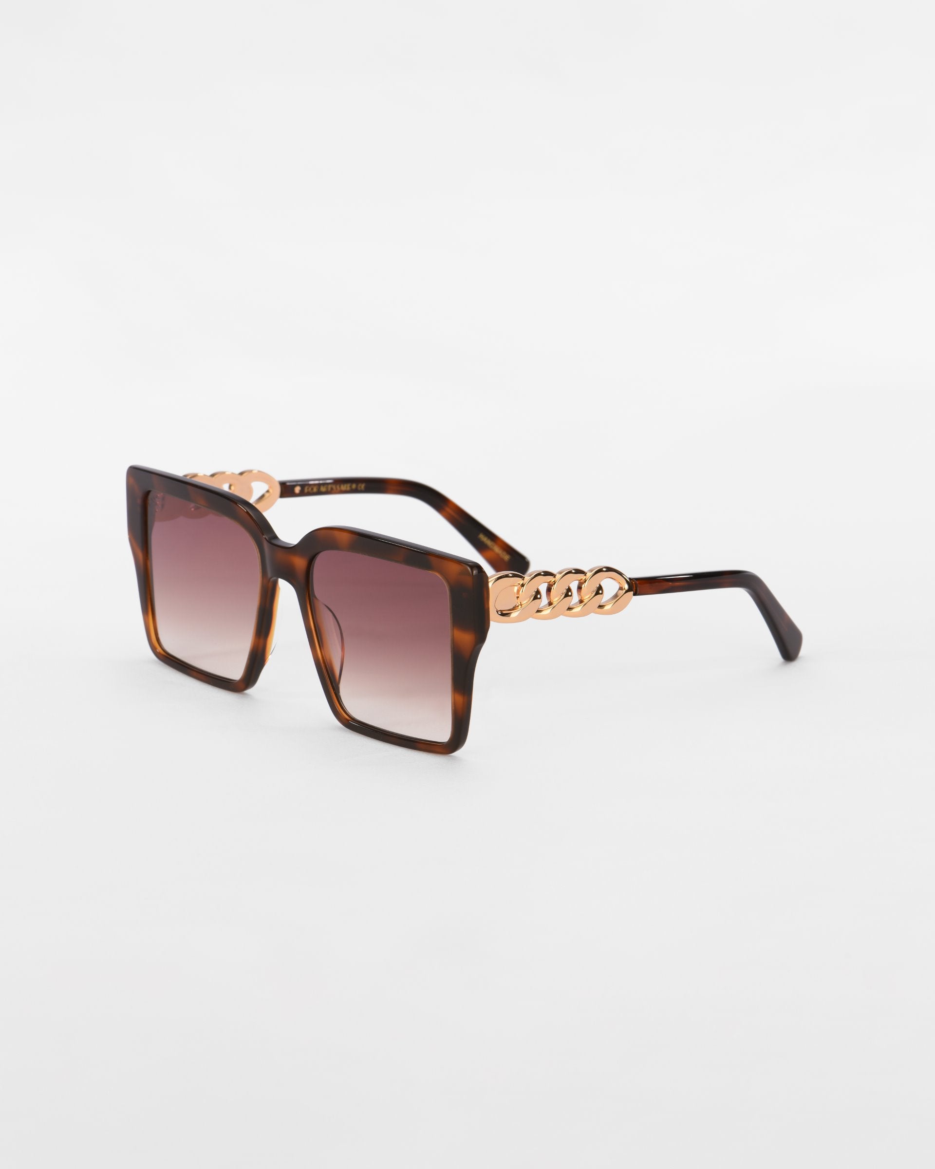 A pair of trendy, oversized square frames with a tortoiseshell finish. The arms showcase luxurious 18-karat gold plated chain-link detailing near the hinges. Ultra-lightweight lenses offer a gradient from dark to light. The white background emphasizes the stylish design of the Castle by For Art&#39;s Sake®.