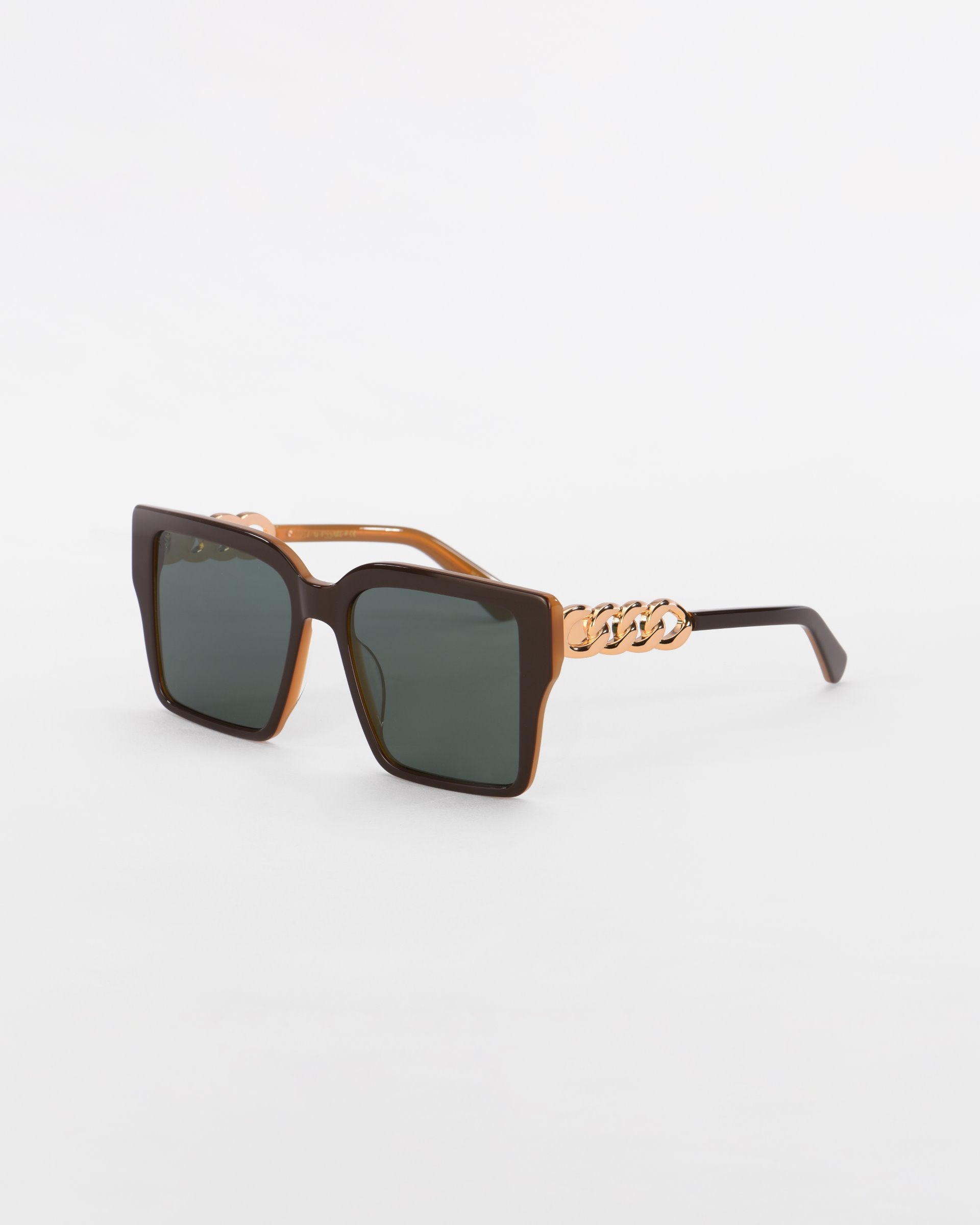 A pair of Castle sunglasses from For Art&#39;s Sake® with oversized square black lenses and thick brown gradient frames. The temples feature an 18-karat gold plated chain-link detail near the hinges, adding a touch of luxury. The background is a simple white.
