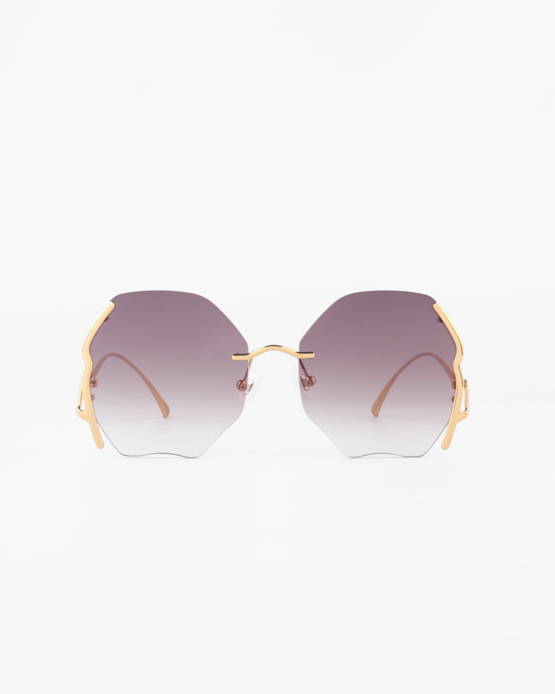 A front view of For Art's Sake® Century sunglasses with hexagonal lenses that have a gradient from dark purple to clear. The gold-plated stainless steel frames feature minimalist design with gold accents on the sides. These stylish shades offer 100% UVA & UVB protection against harmful rays. The background is plain white.