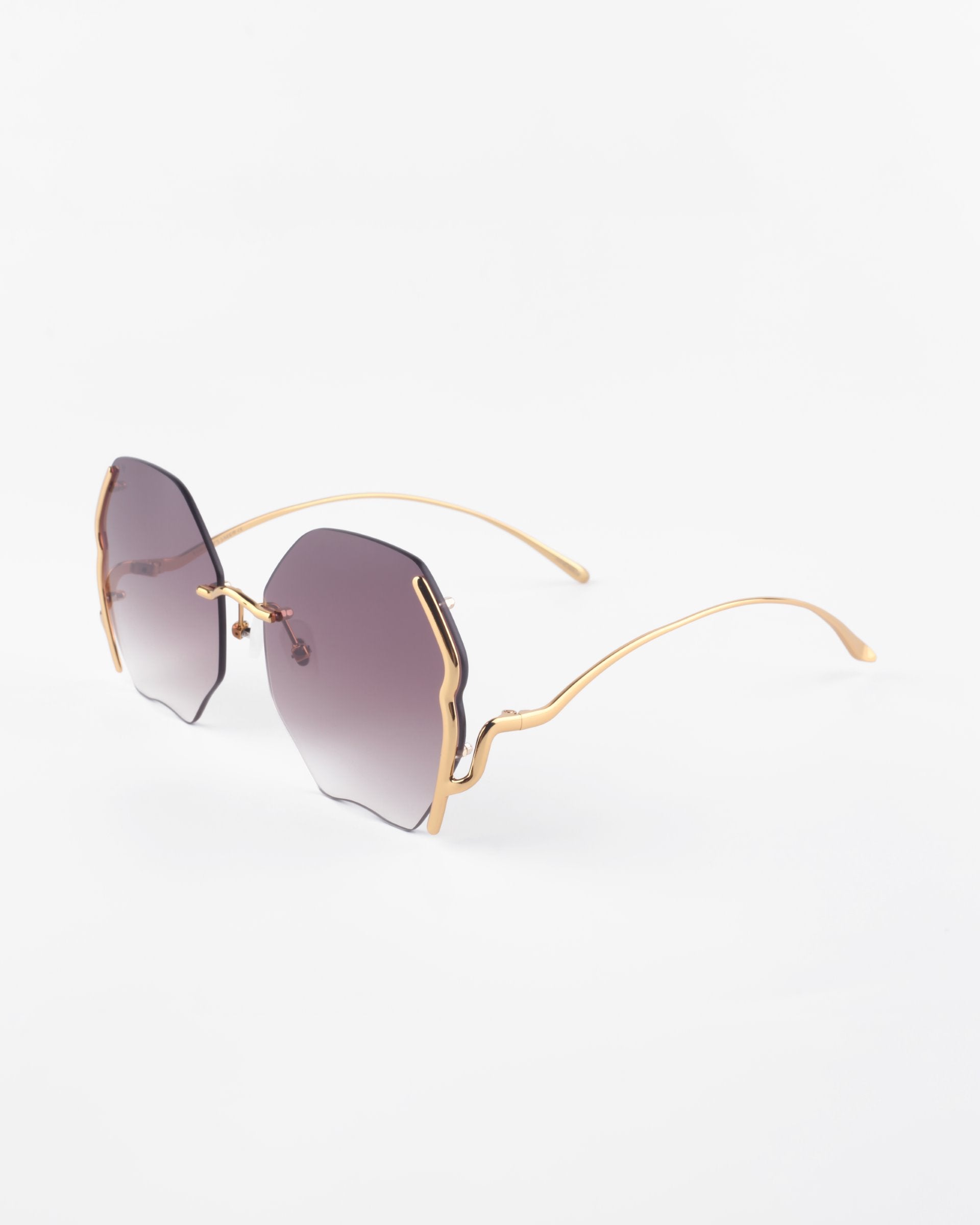 A pair of Century sunglasses from For Art&#39;s Sake® with irregularly shaped, lightly tinted lenses and thin, gold-plated stainless steel frames. The lenses have a gradient from dark to light tint, offering 100% UVA &amp; UVB protection. The overall design is modern and stylish.