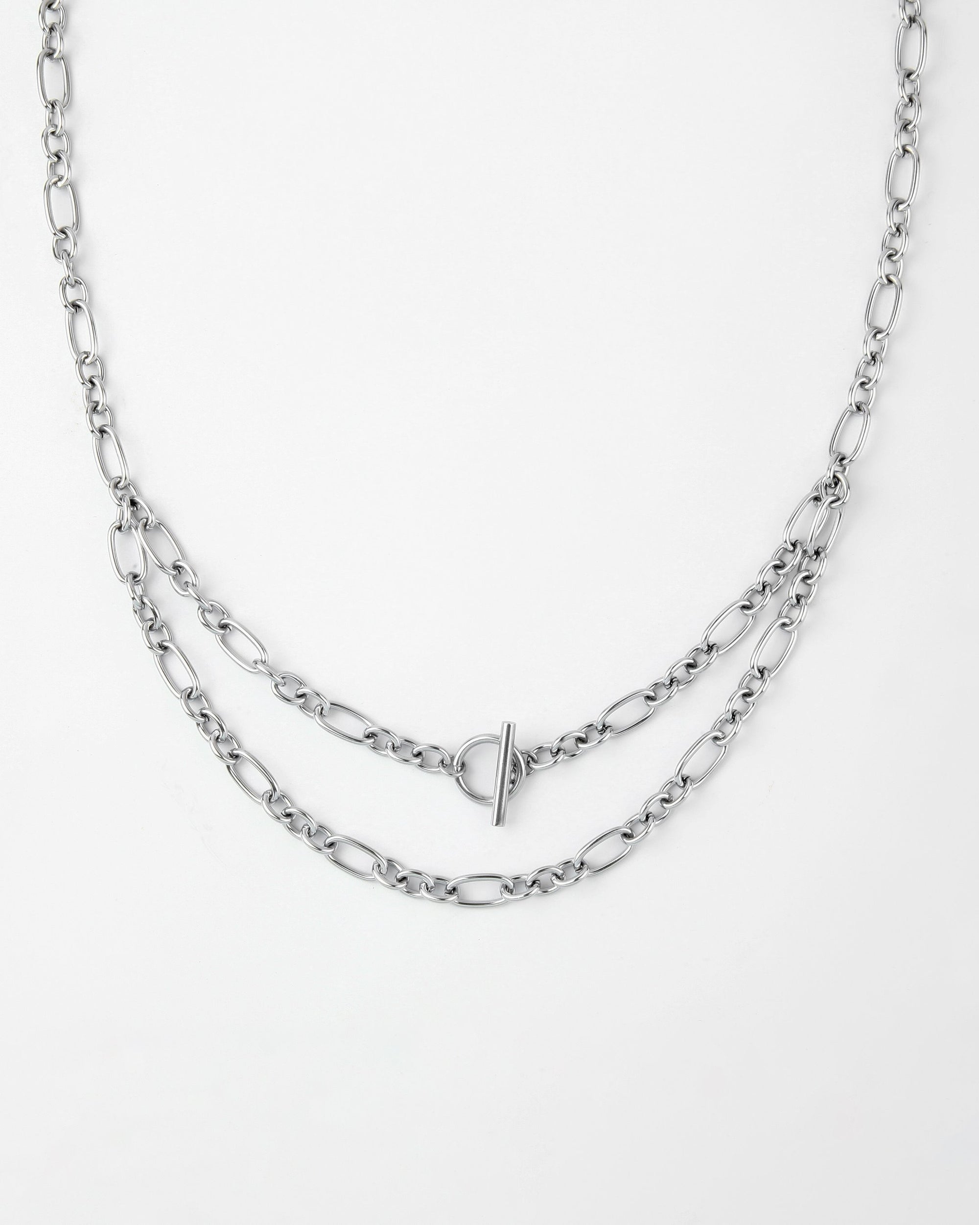 A Clio Glasses Chain from For Art's Sake® with two layers of links is pictured on a white background. The chain features a T-bar clasp positioned at the front, adding a subtle decorative element. The links vary slightly in size, creating a delicate yet intricate design characteristic of layered chains.