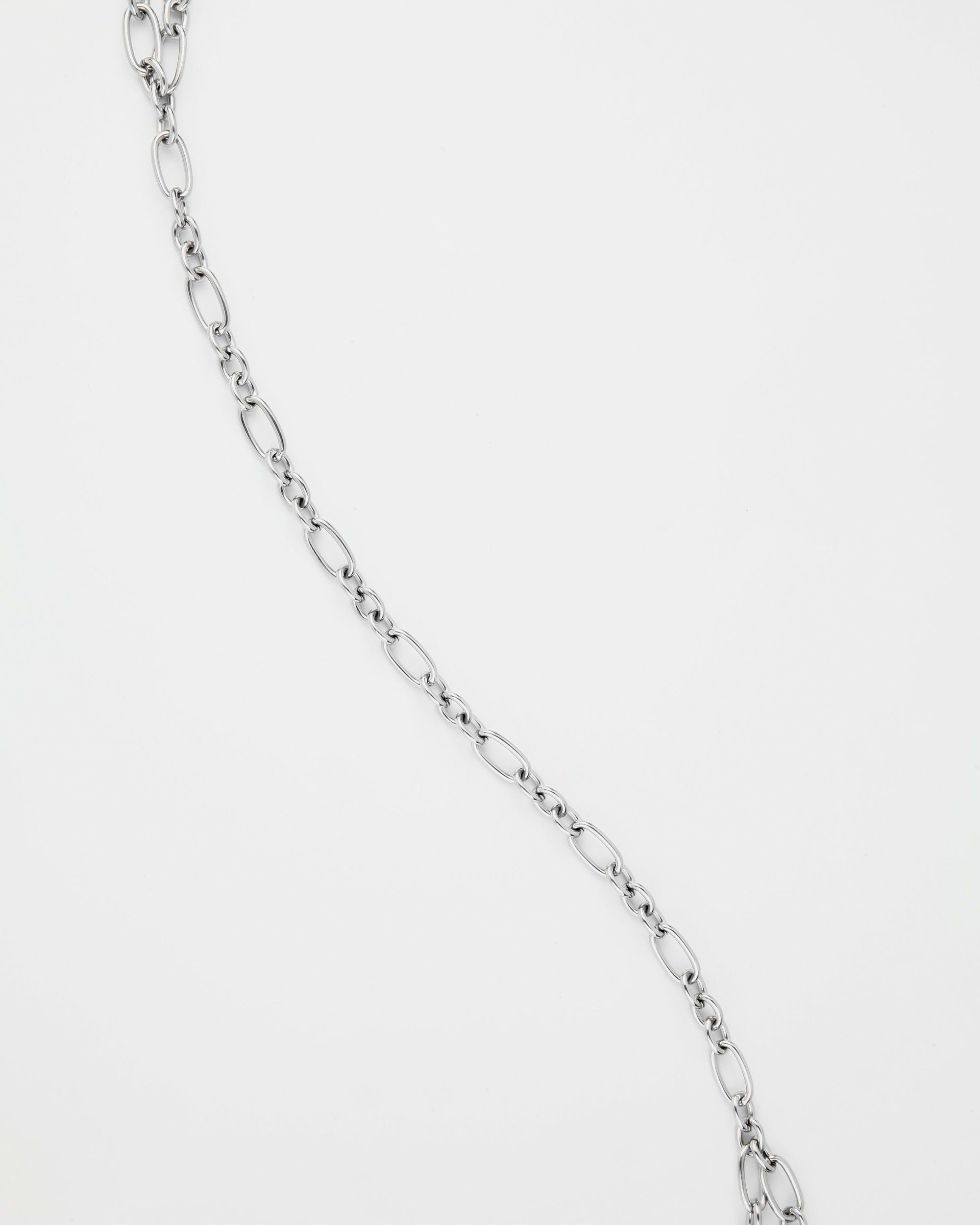 A thin, silver For Art's Sake® Clio Glasses Chain with oval links arranged in an elongated pattern against a plain white background. The chain, perfect for layered necklaces, has a simple and elegant design that reflects light subtly.