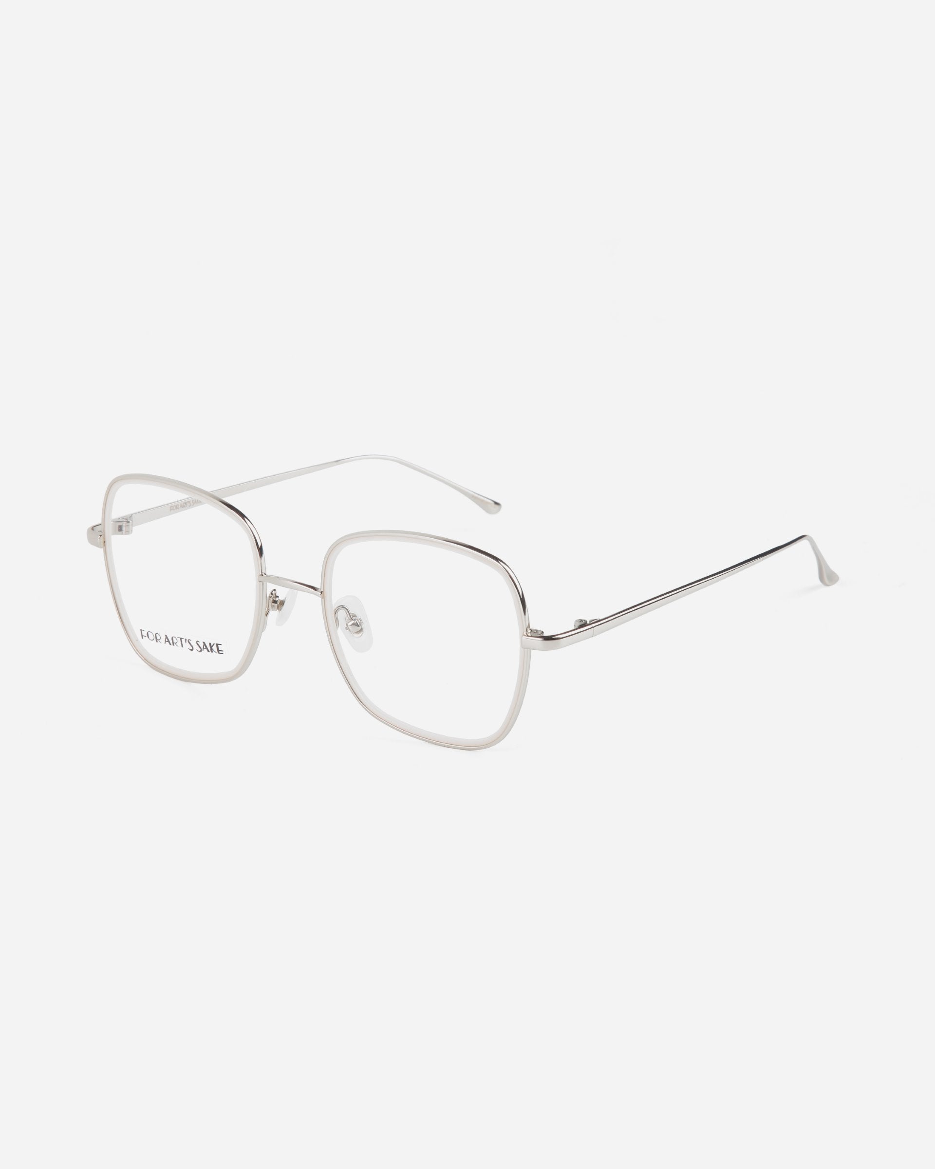A pair of rectangular, thin, silver-framed Coconut eyeglasses from For Art&#39;s Sake® with clear, ultra-lightweight lenses. The left lens has text that reads &quot;ECO ARTS SAVE.&quot; The glasses are viewed at an angle against a white background.