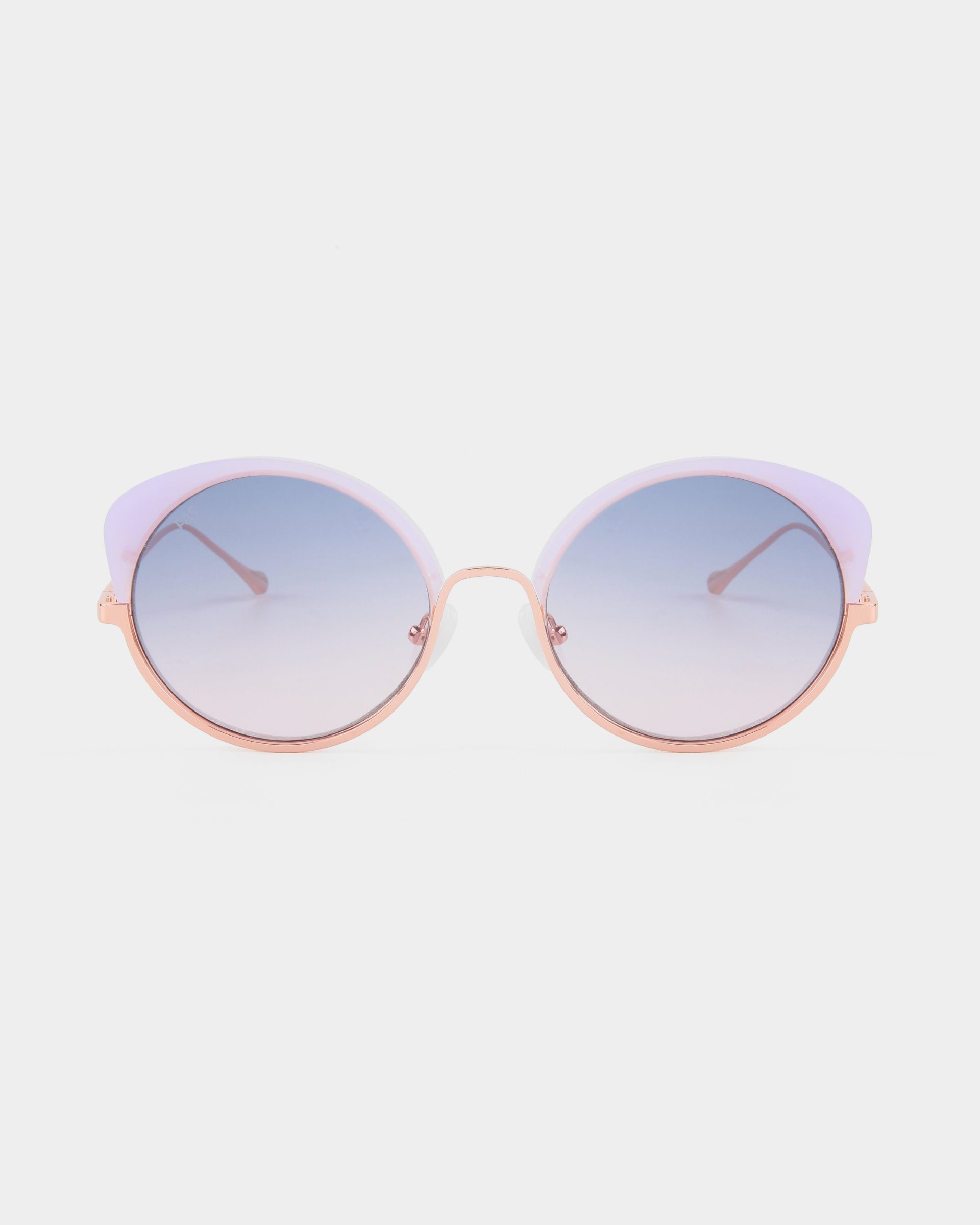 A pair of Cocoon sunglasses from For Art&#39;s Sake® with a gradient lens from blue to clear. The frame is a blend of gold and light purple, with thin gold arms. These handcrafted eyewear pieces offer UV protection and are displayed against a white background.
