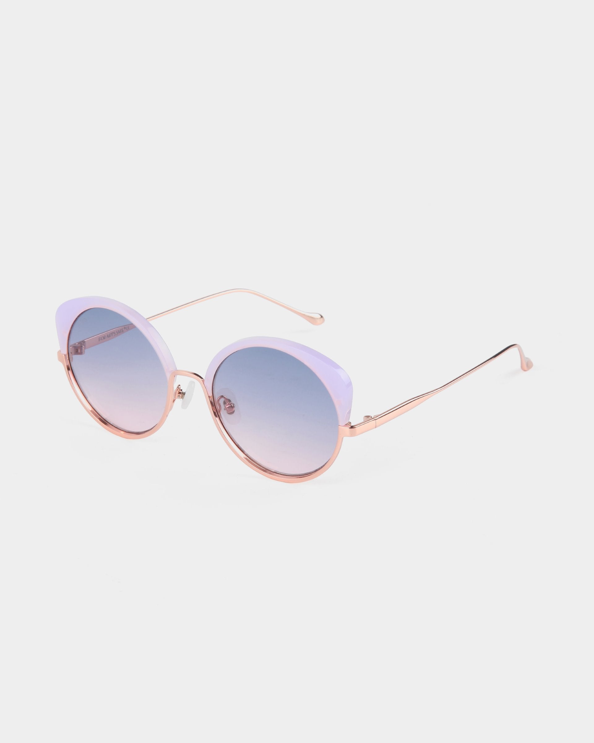 A pair of stylish, handcrafted Cocoon cat-eye sunglasses by For Art&#39;s Sake® with light purple frames and rose gold temples. The lenses are round with a gradient tint that transitions from purple to clear, offering essential UV protection. The Cocoon sunglasses by For Art&#39;s Sake® rest elegantly on a white surface.