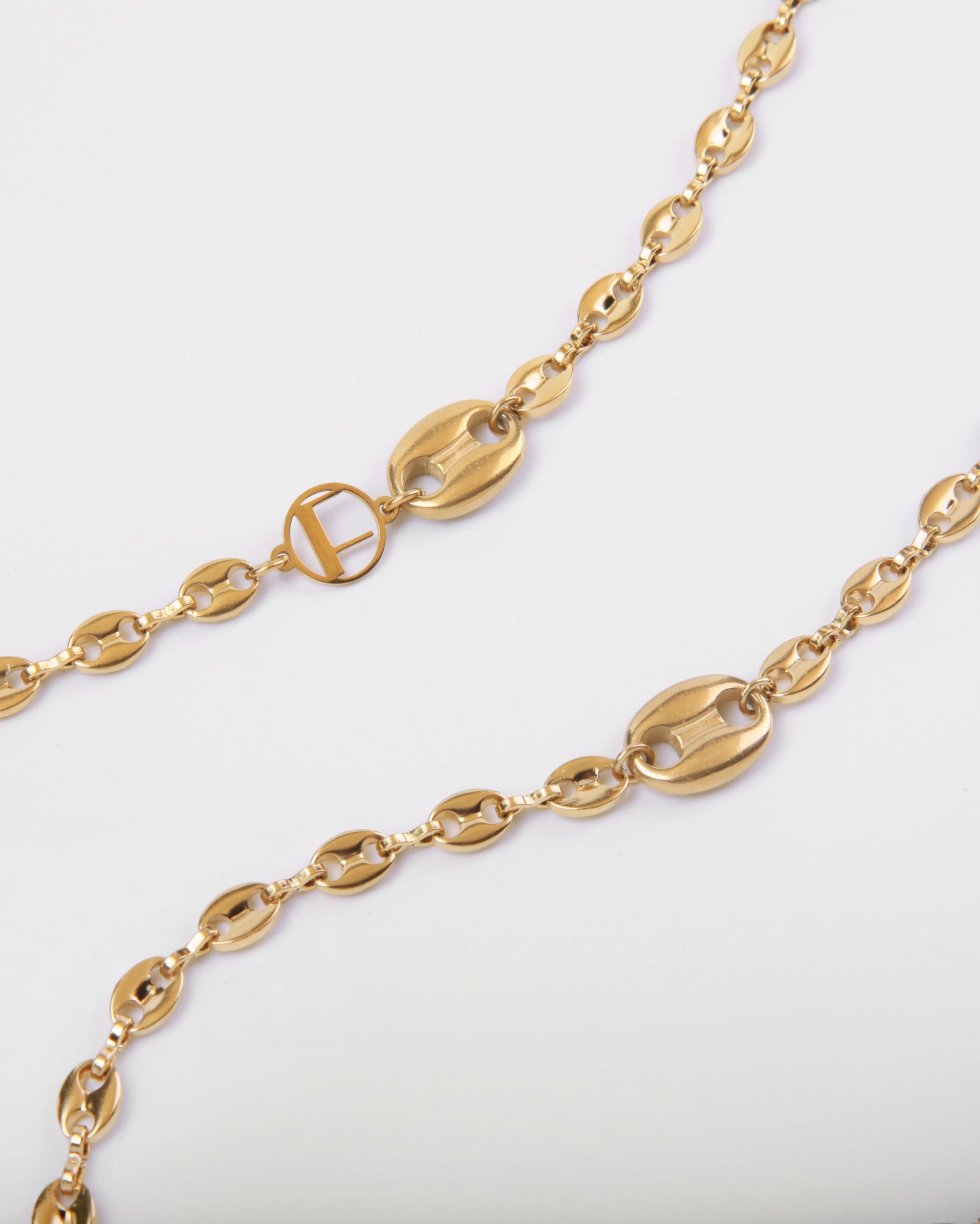 A close-up image of a For Art's Sake® Coral Glasses Chain featuring a gold-plated chain with an intricate design. The chain boasts oval-shaped links with solid connector pieces and circular interlocking segments, creating an elegant and luxurious look on a white background.