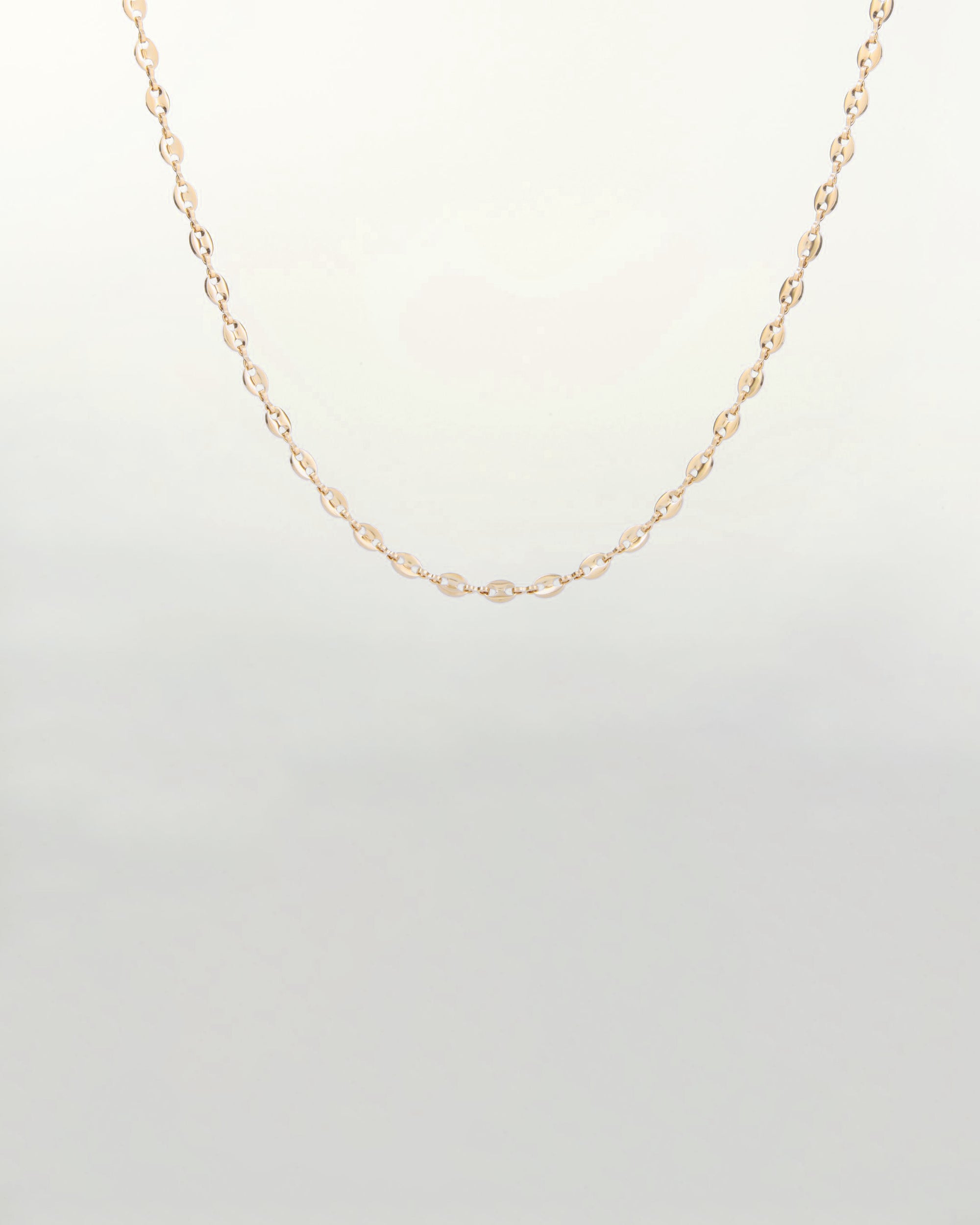 A delicate 18-karat gold-plated Coral Glasses Chain by For Art's Sake® with small, closely linked oval-shaped links, hanging against a plain light background. The simplicity of the design gives it an elegant and timeless appearance, reminiscent of an abstract cowry shell design.