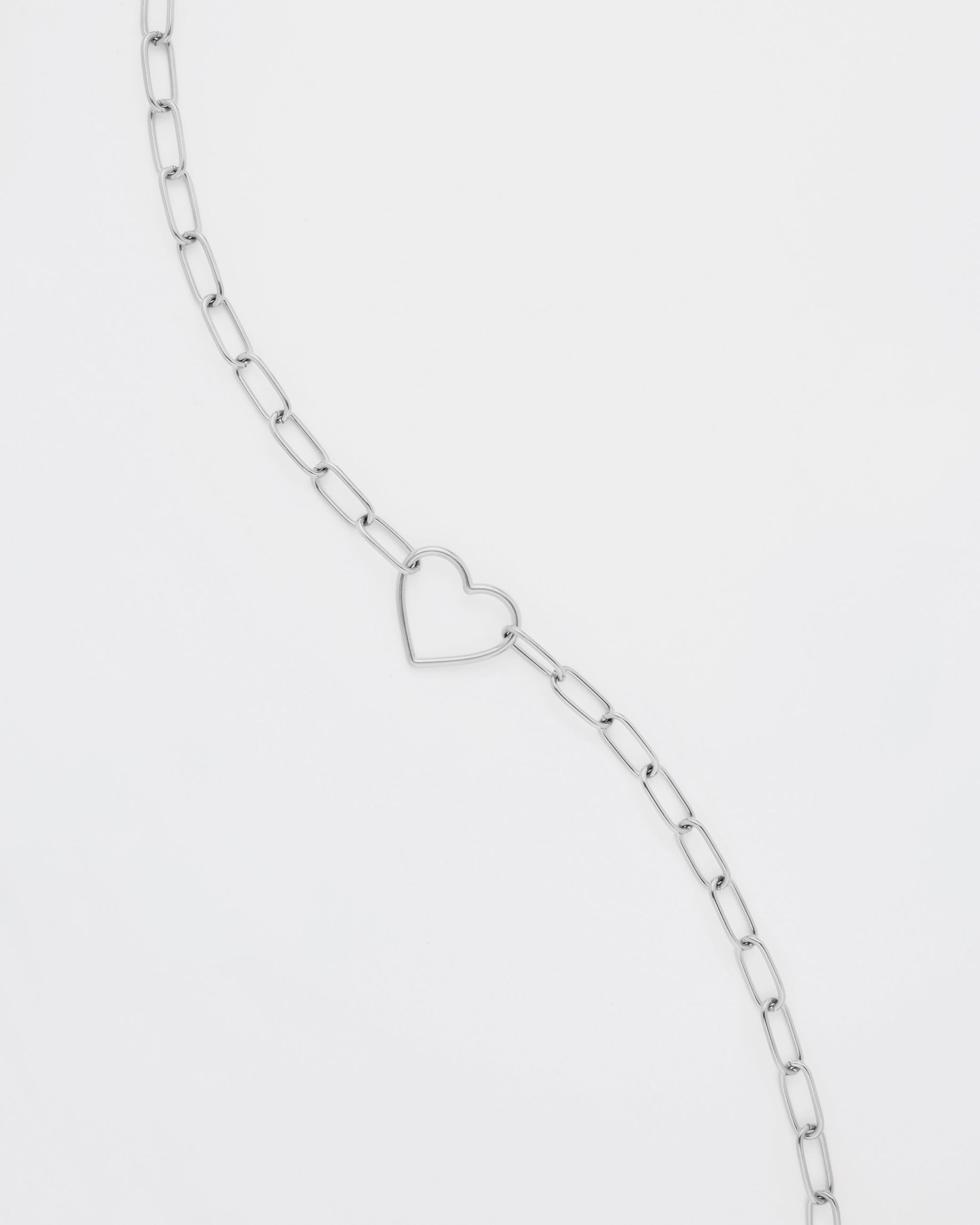 A delicate Cupid Glasses Chain featuring rectangular links with an open heart-shaped pendant in the center, arranged diagonally against a plain white background by For Art's Sake®.