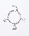 The Daisy Bracelet by For Art's Sake® is a silver and gold tone charm bracelet adorned with a starfish, a small flower outline, and a rose featuring a pearl at its center. It showcases a series of interconnected links and fastens with a lobster clasp.