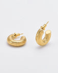 A pair of 24k gold hoop earrings with a ribbed, cylindrical design are shown against a plain white background. The Daisy Earrings Gold by For Art's Sake® have post backings.