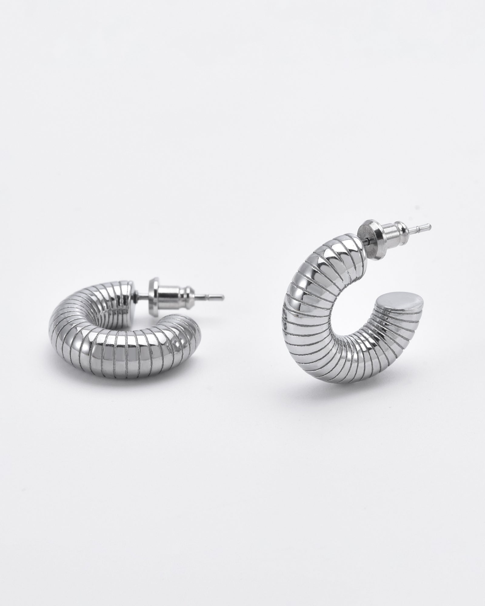 A pair of Daisy Earrings Silver by For Art's Sake® are shown against a plain white background. The earrings have a coiled design, resembling springs, and are slightly open at the ends where the earring posts and backs are visible. Hypoallergenic and sleek, the overall design is modern and minimalist.