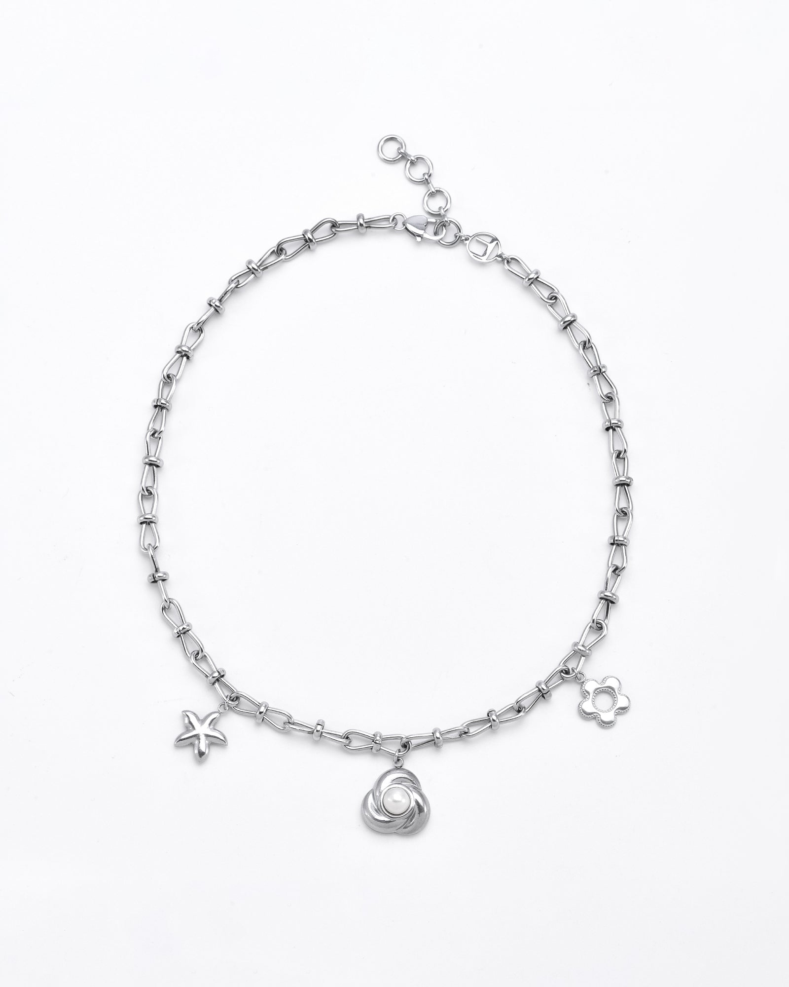 The For Art's Sake® Daisy Necklace Silver is a delicate silver chain necklace featuring three small charms: a star, a circular swirl, and a flower. The chain has a lobster clasp with an adjustable extender for length. Each charm is accented with 24-karat gold plating, creating a subtle contrast against the plain white background.