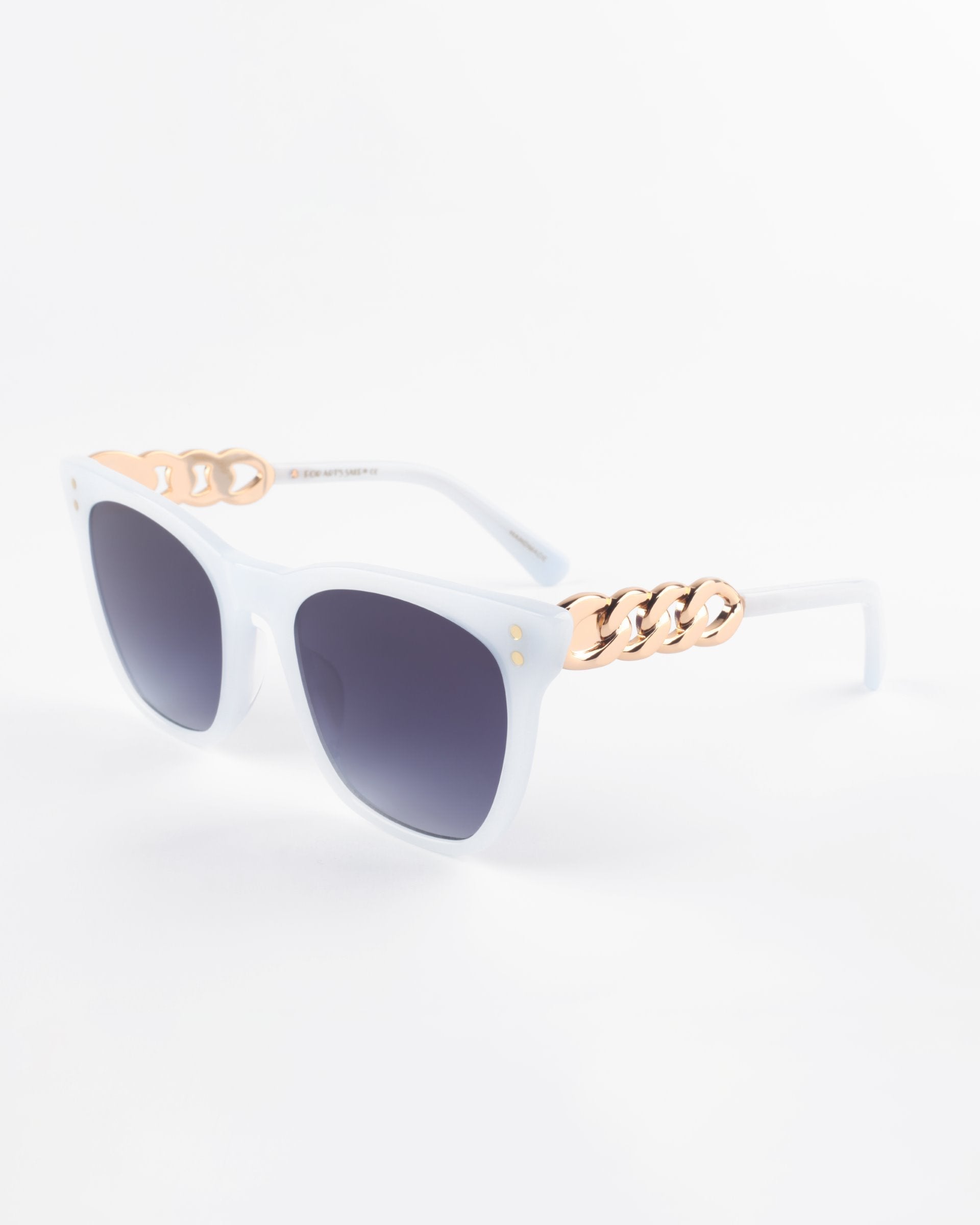 A pair of white cat-eye sunglasses with dark lenses and gold chain-link accents on the temples. The acetate frame has a glossy finish, and the Deco sunglasses by For Art&#39;s Sake® are set against a plain white background.