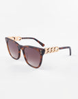 A pair of stylish Deco cat-eye sunglasses by For Art's Sake® with tortoiseshell acetate frames and dark lenses. The arms of the Deco sunglasses feature a distinctive gold chain link design near the hinges. The background is plain white.