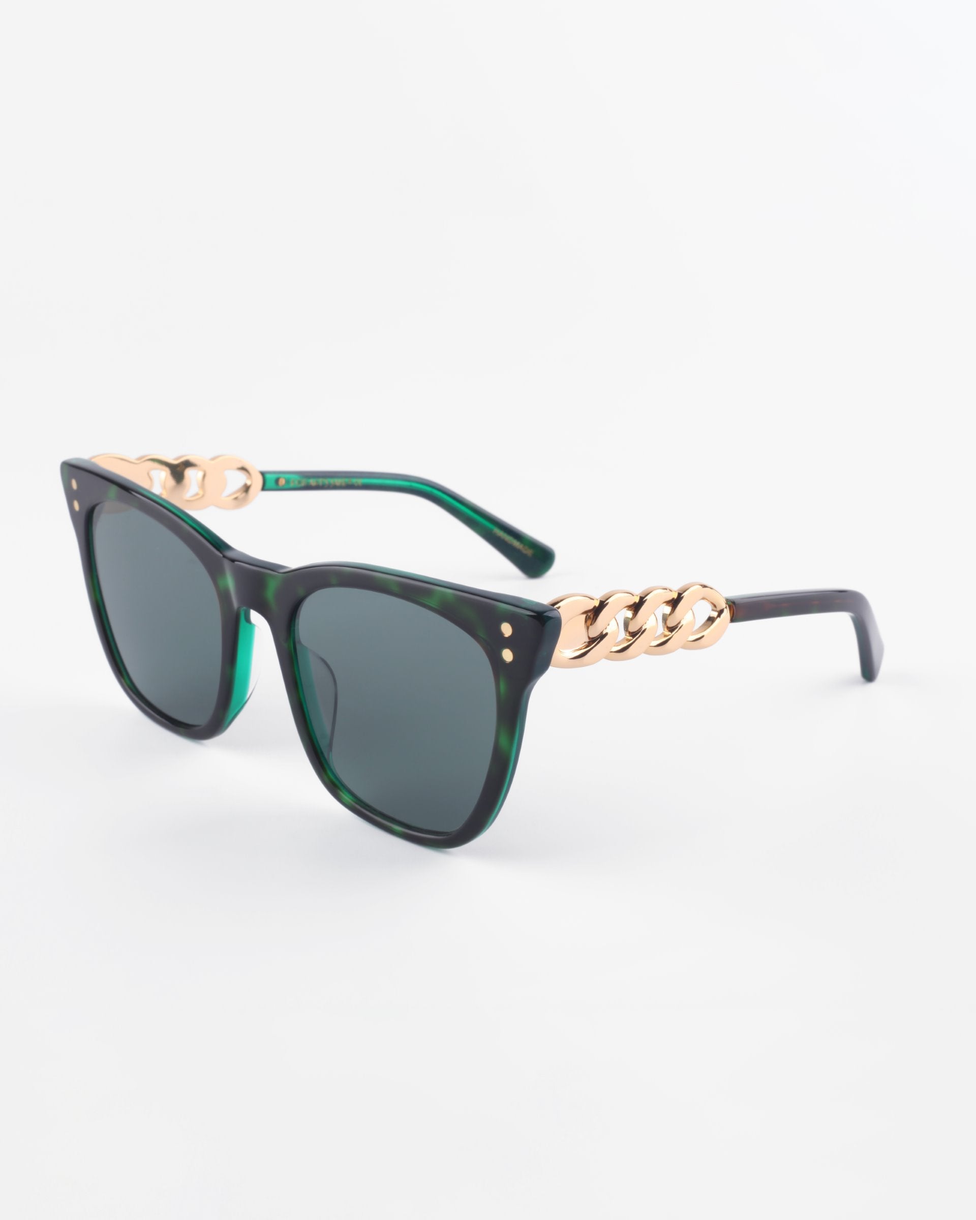 A pair of stylish, square-shaped Deco sunglasses from For Art&#39;s Sake® with dark lenses and green tortoiseshell acetate frames. The frames feature gold-colored chain link details at the temples, adding an elegant touch to the design. The background is plain white, highlighting the Deco sunglasses from For Art&#39;s Sake®.