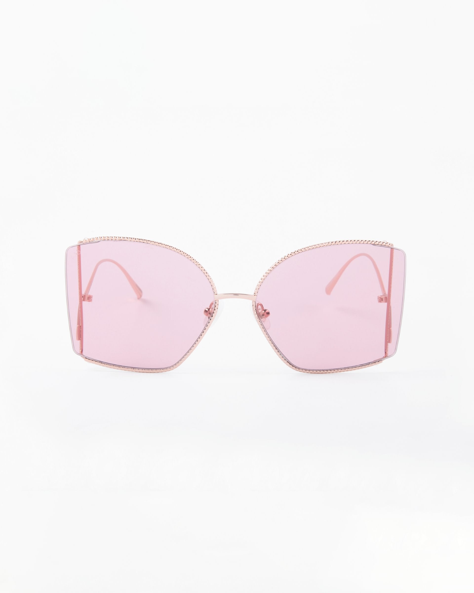 A pair of Dixie oversized, square-framed sunglasses with pink-tinted, shatter-resistant nylon lenses and thin, handmade gold-plated temples by For Art's Sake®. The design is minimalistic with a modern and stylish aesthetic that also offers UV protection. The background is plain white.