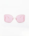 A pair of Dixie oversized, square-framed sunglasses with pink-tinted, shatter-resistant nylon lenses and thin, handmade gold-plated temples by For Art's Sake®. The design is minimalistic with a modern and stylish aesthetic that also offers UV protection. The background is plain white.