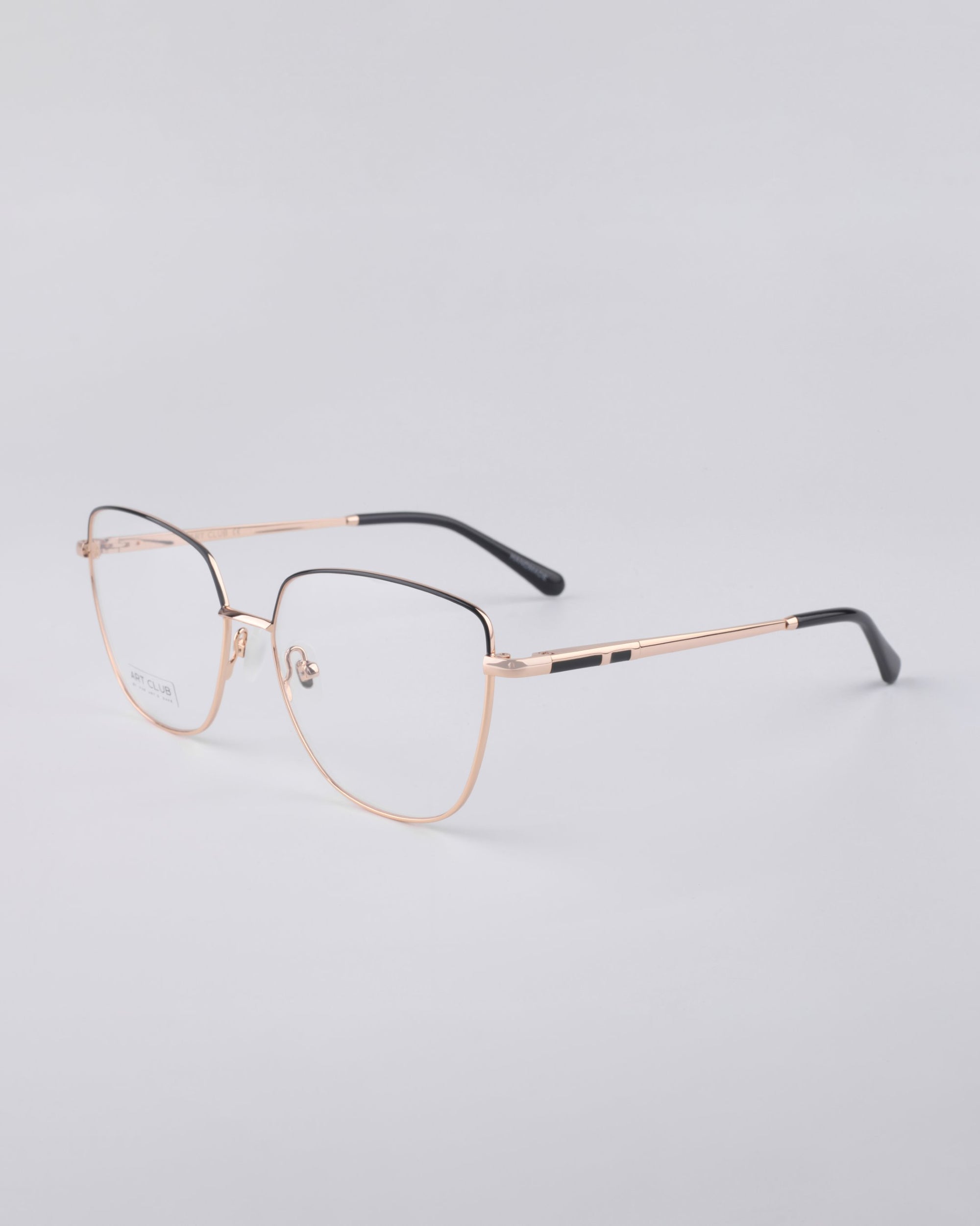 Showcased against a plain, light gray background are the elegant Dora frames from For Art's Sake®, boasting a sleek design with thin rose gold metal frames and black temple tips. These frames feature clear lenses equipped with a blue light filter, exuding both minimalist sophistication and modern style.