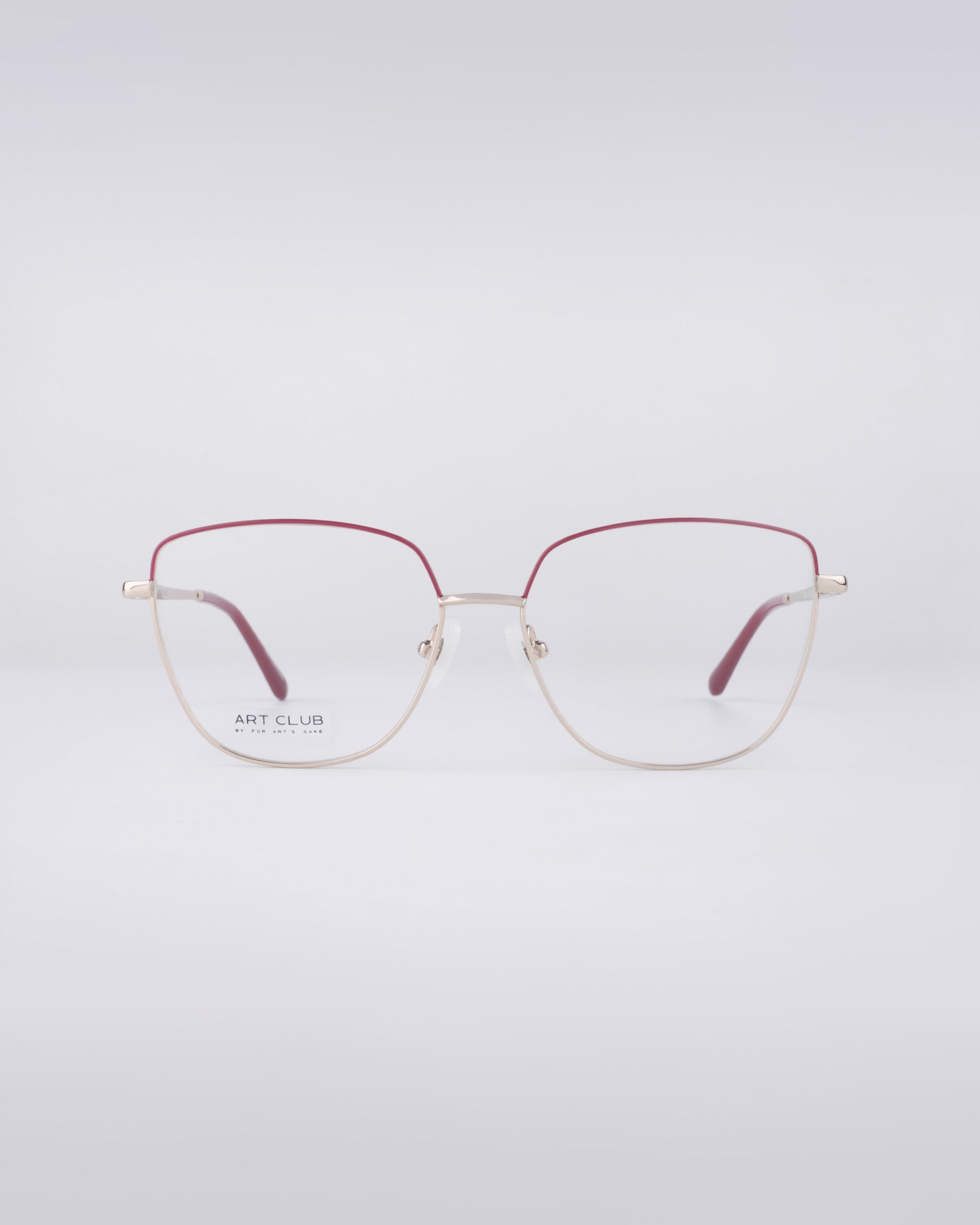 A pair of Dora eyeglasses from For Art's Sake® showcases a sleek design with thin metal frames and a robust stainless steel core. The muted red top half beautifully contrasts with the gold-tone bottom, creating a refined look. These fashionable glasses are fitted with blue light filter lenses that remain clear for any occasion. Set against a simple light gray backdrop, they exude elegance.