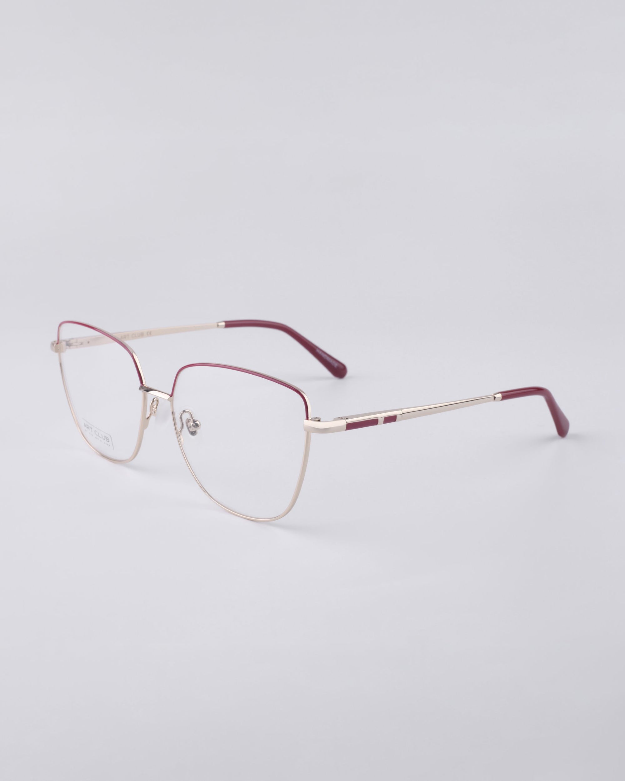 The Dora frames from For Art's Sake® showcase a sleek, metallic gold design with maroon temple tips set against a plain white backdrop. Equipped with blue light filter lenses, these eyeglasses effortlessly combine minimalist and modern aesthetics.