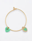 A minimalistic, delicate Double Heart Bracelet Gold featuring two heart-shaped charms by For Art's Sake®. One charm is a smooth, solid green heart, while the other is a decorated gold heart with a green center. The 24k gold plating adds an extra touch of elegance. The bracelet is set against a plain white background.