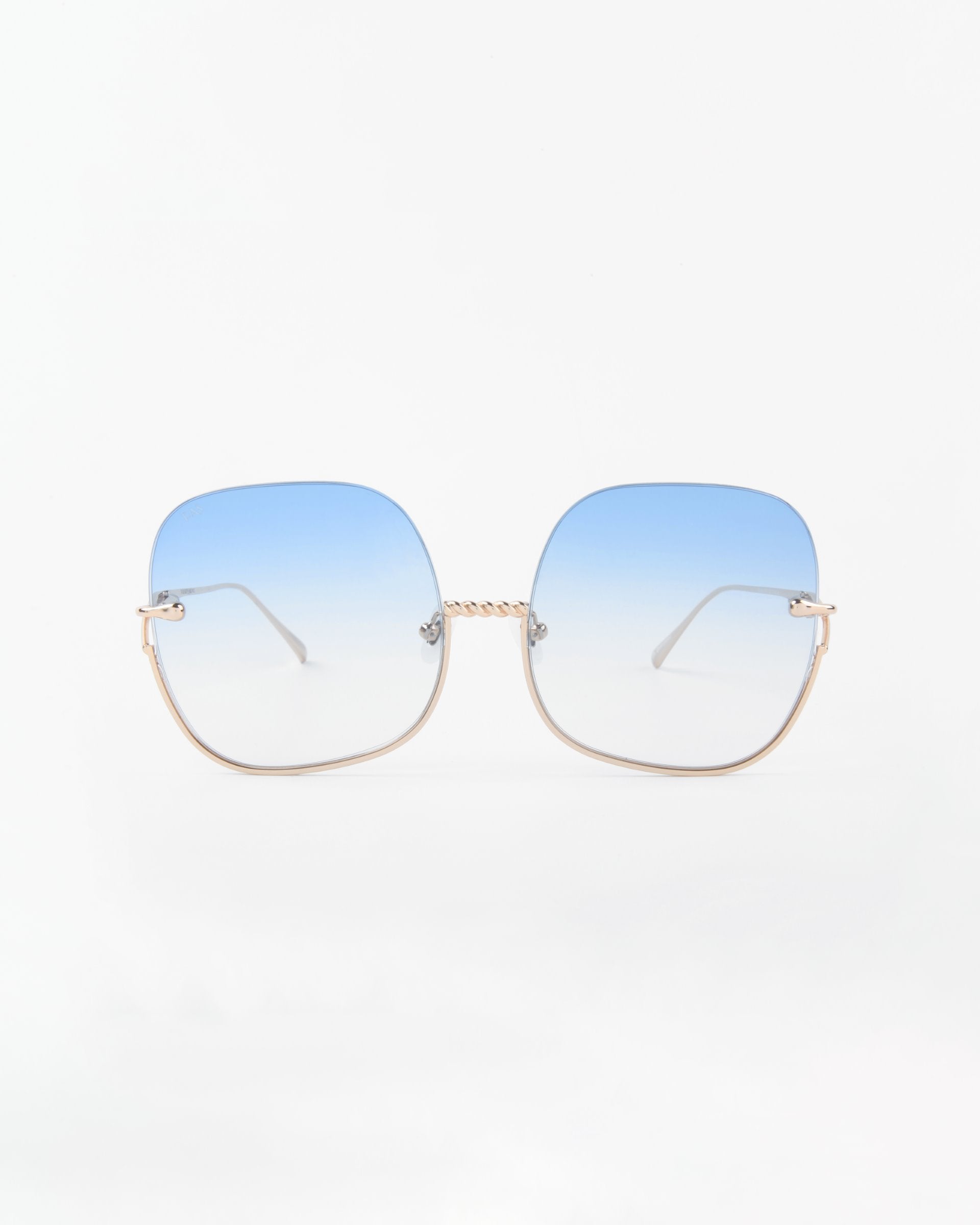 A pair of sunglasses with large, square, shatter-resistant lenses that gradient from blue at the top to clear at the bottom. They feature a handmade gold-plated frame with a delicate twisted design on the nose bridge and slim gold temples. The lenses offer UVA & UVB protection. The background is plain white. These are the Duchess by For Art's Sake®.