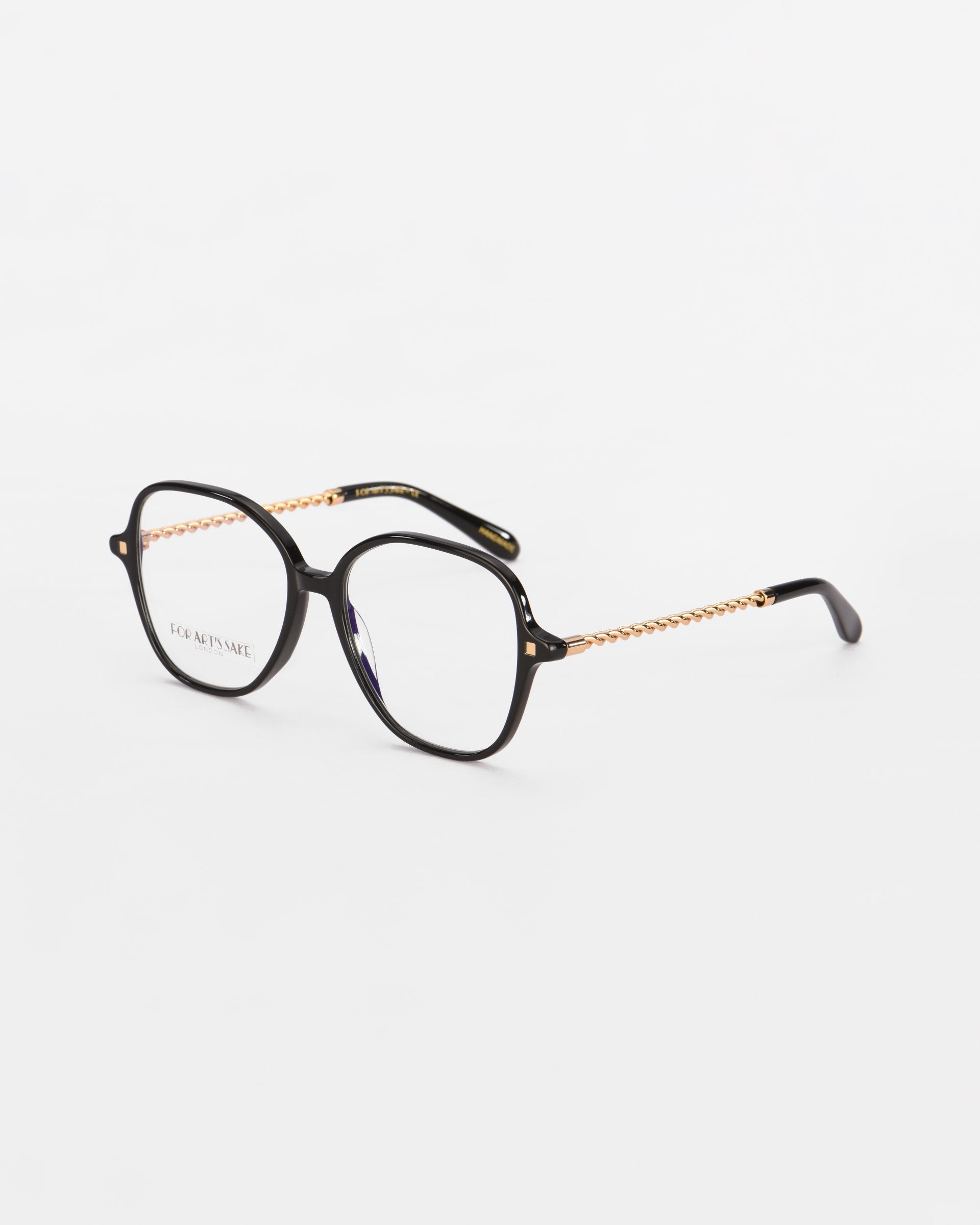 A pair of black Dumpling eyeglasses with a square frame and gold arms by For Art&#39;s Sake®. The arms have a decorative chain-like pattern. The lenses offer blue light filter protection. The glasses are placed on a white surface.