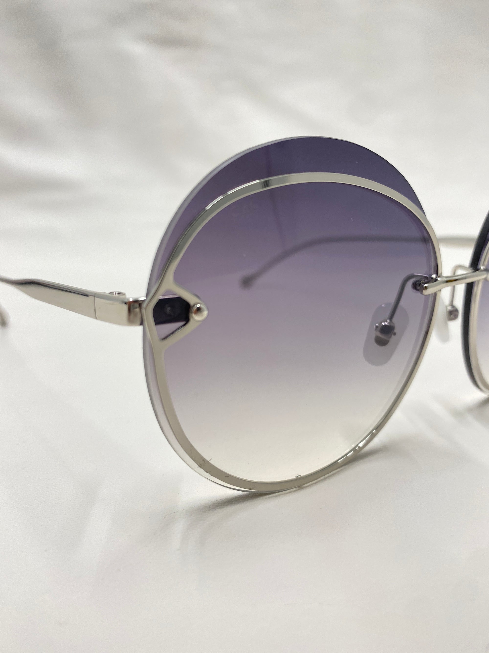 Close-up of the Quartz sunglasses from For Art&#39;s Sake®, featuring round, gradient-lensed nylon lenses that transition from a darker shade at the top to a lighter shade at the bottom, and sleek stainless steel frames. The background is white.