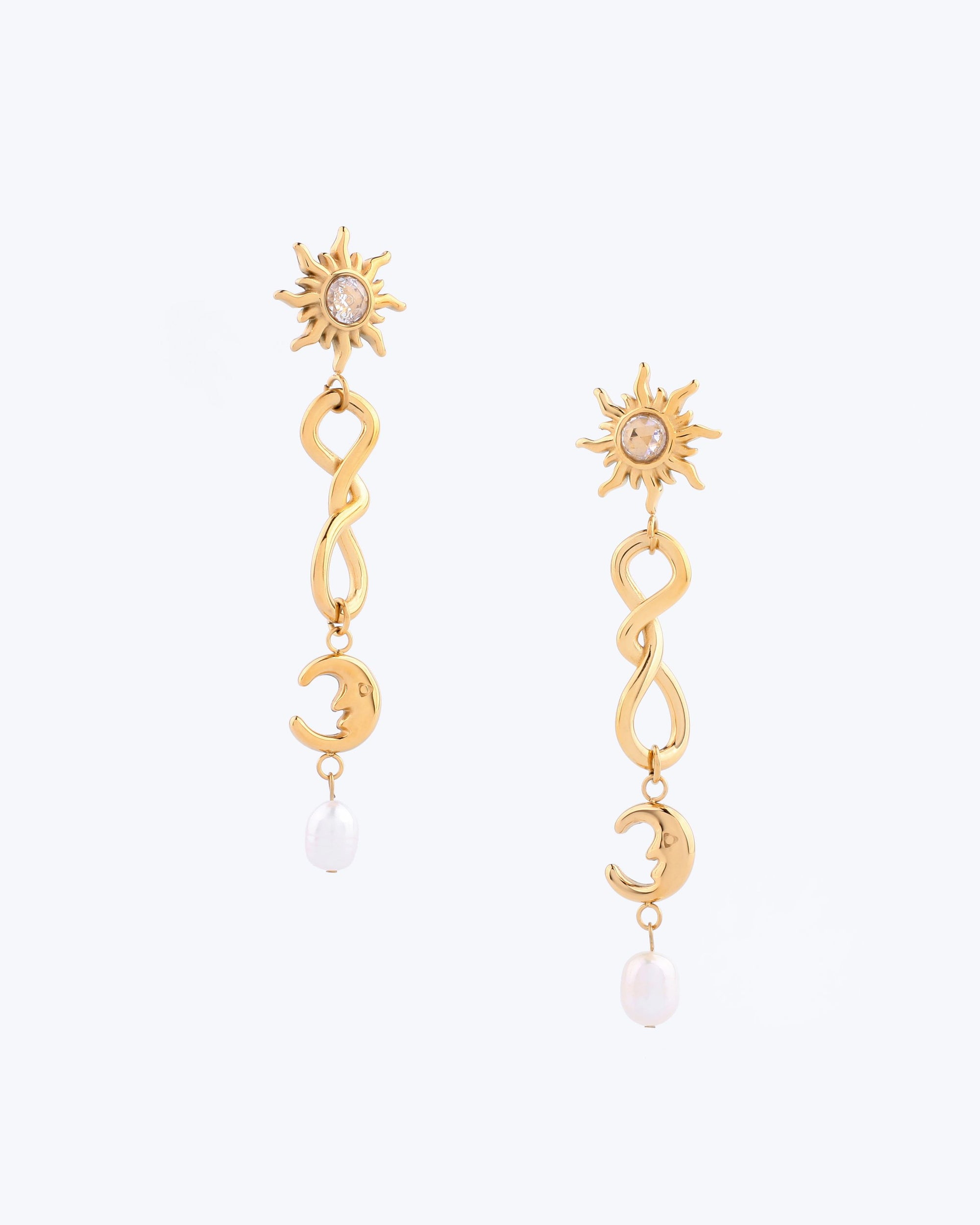 The Sloane Earrings by For Art's Sake® showcase a sun design adorned with a central gem, leading into a twisting structure that culminates in a crescent moon. Each elegant earring features a small pearl dangling at the end, set against a light background for added aesthetic appeal and optimal weight balance, ensuring comfortable wear.