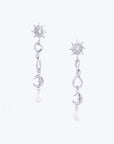 The Sloane Earrings by For Art's Sake® are exquisite silver pieces featuring a sun-shaped stud adorned with a central gemstone. Each earring showcases a wavy design that flows into a crescent moon charm, culminating in a small dangling pearl. Displayed on a light background, these earrings perfectly blend elegance and charm.