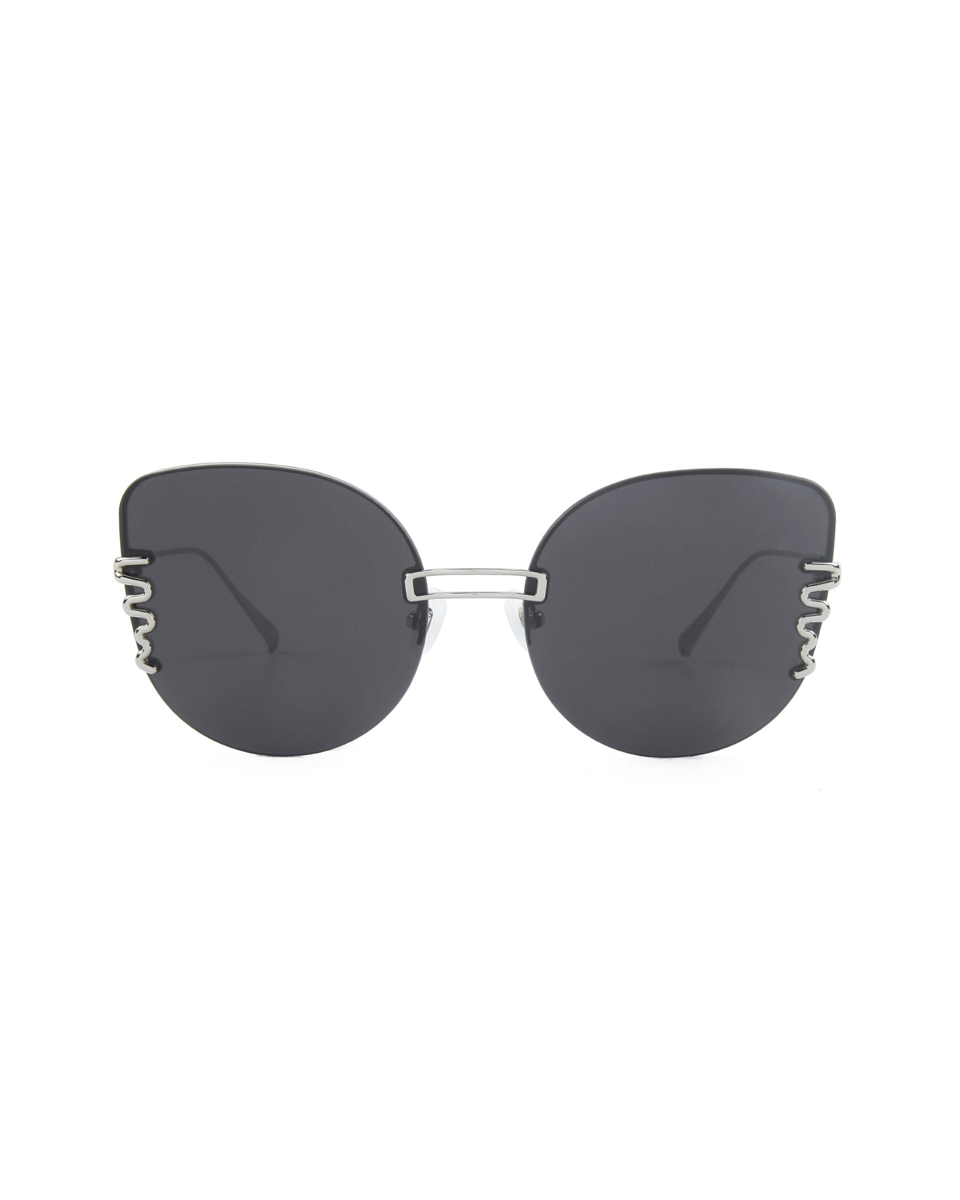 A pair of stylish, oversized cat-eye sunglasses with dark lenses and a unique frame design. The frames feature a silver metal bridge and decorative silver elements on the outer edges of the lenses, adding a touch of elegance to the overall minimalist look. Plus, they offer 100% UV protection. These are the Girlboss by For Art's Sake®.