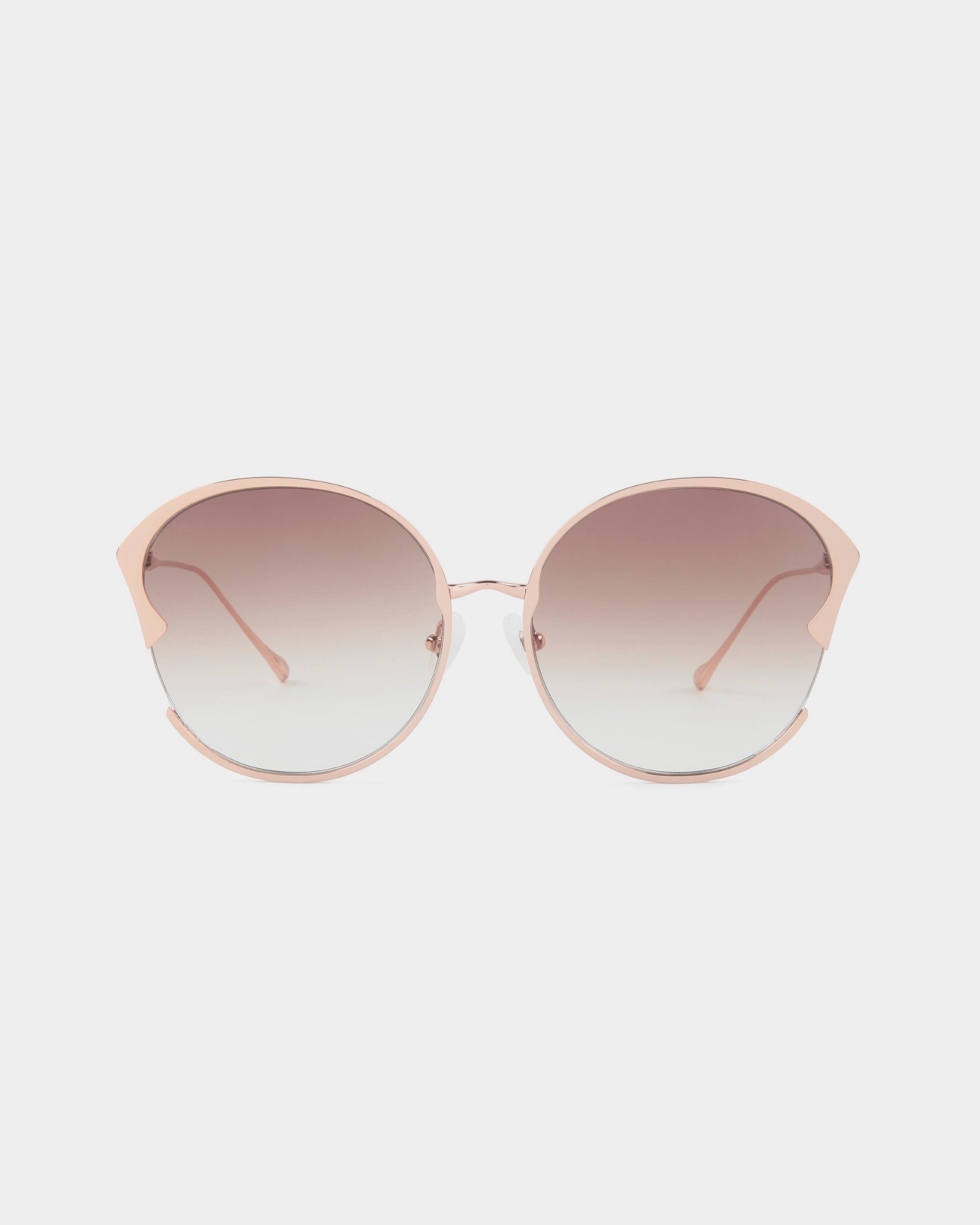 A pair of stylish For Art's Sake® Alectrona sunglasses with large, round, gradient lenses transitioning from dark to light shades. The frame is a light pink metal with a subtle cat-eye shape, featuring 18-karat gold-plated temples that are slim and matching in color. The background is white.